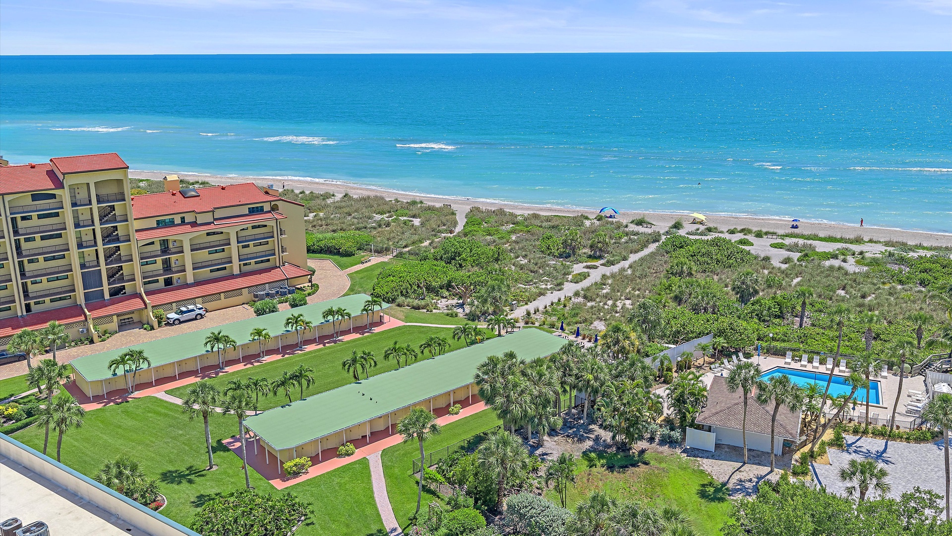 Beachfront property features lush landscaped grounds, a sparkling pool, and direct access to sandy shores along turquoise waters.