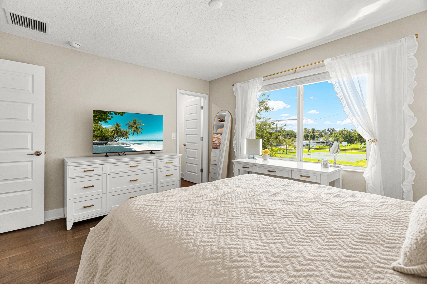 Wake up to peaceful views of open green space from your airy bedroom, where elegant white furnishings and flowing curtains create a serene retreat.