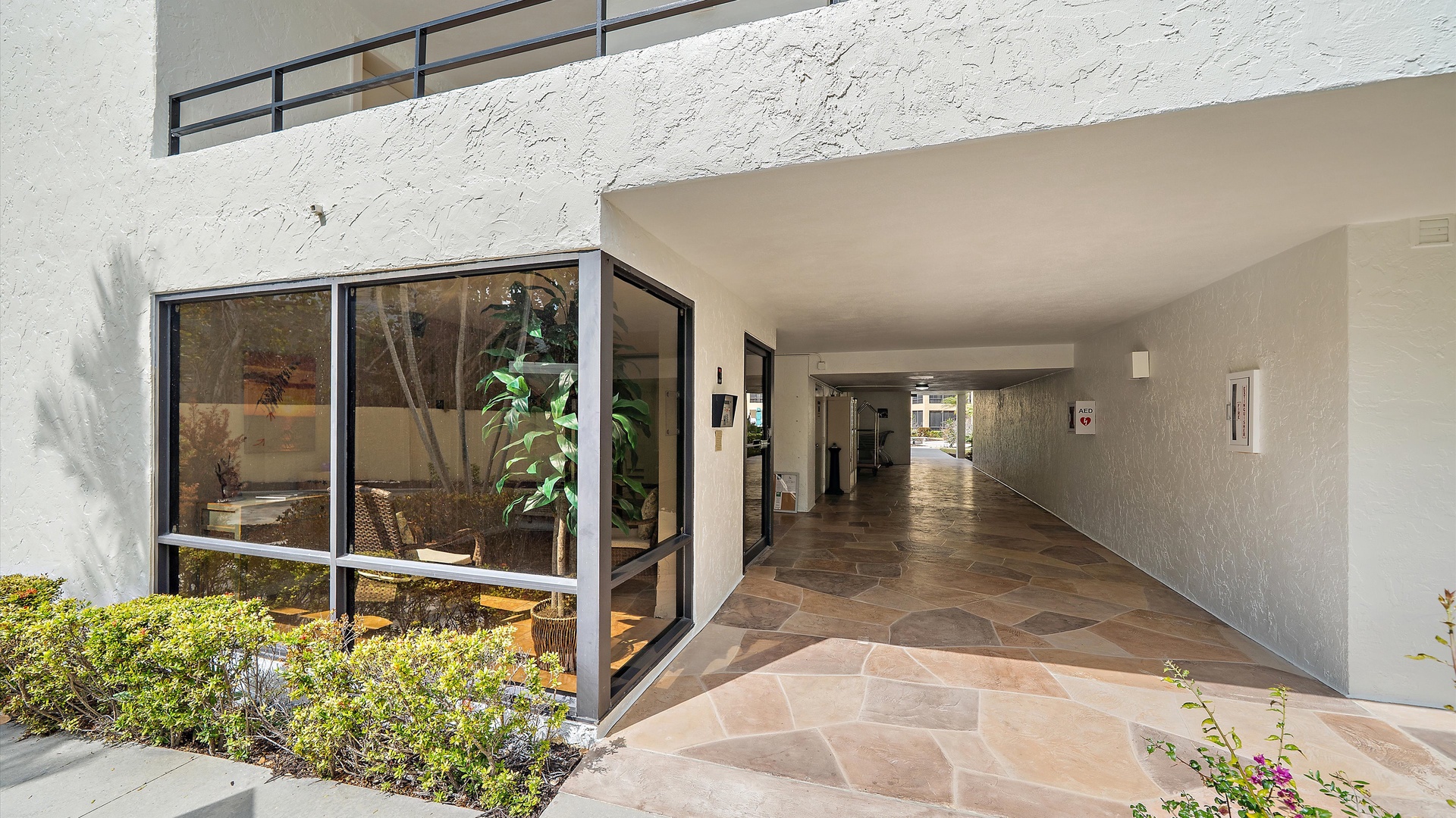 Modern property entrance features stone flooring and glass-walled courtyard area with lush greenery.