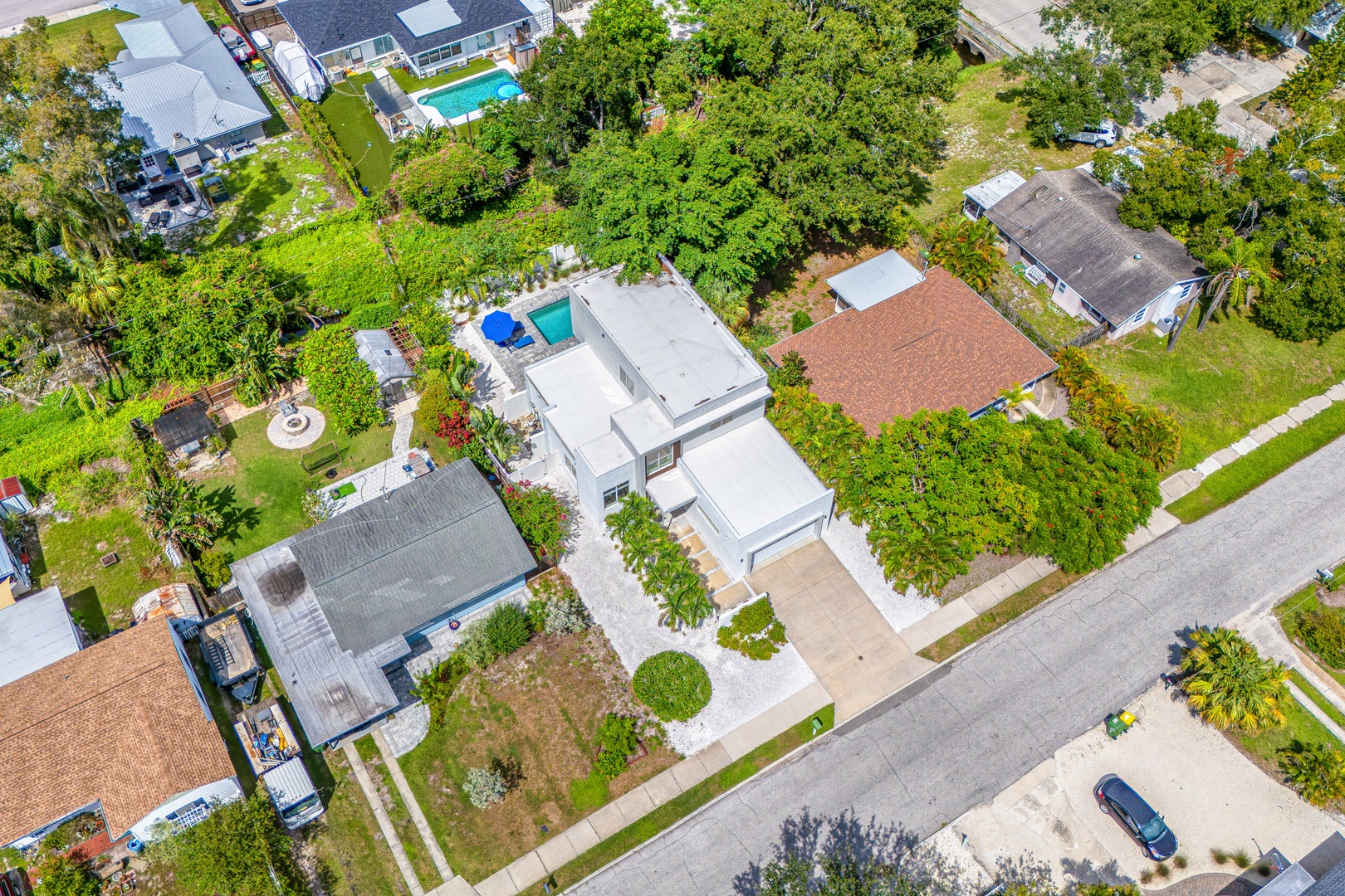 Aerial view of the property nestled in a quiet, tree-lined neighborhood with a private pool and lush greenery surrounding the home.