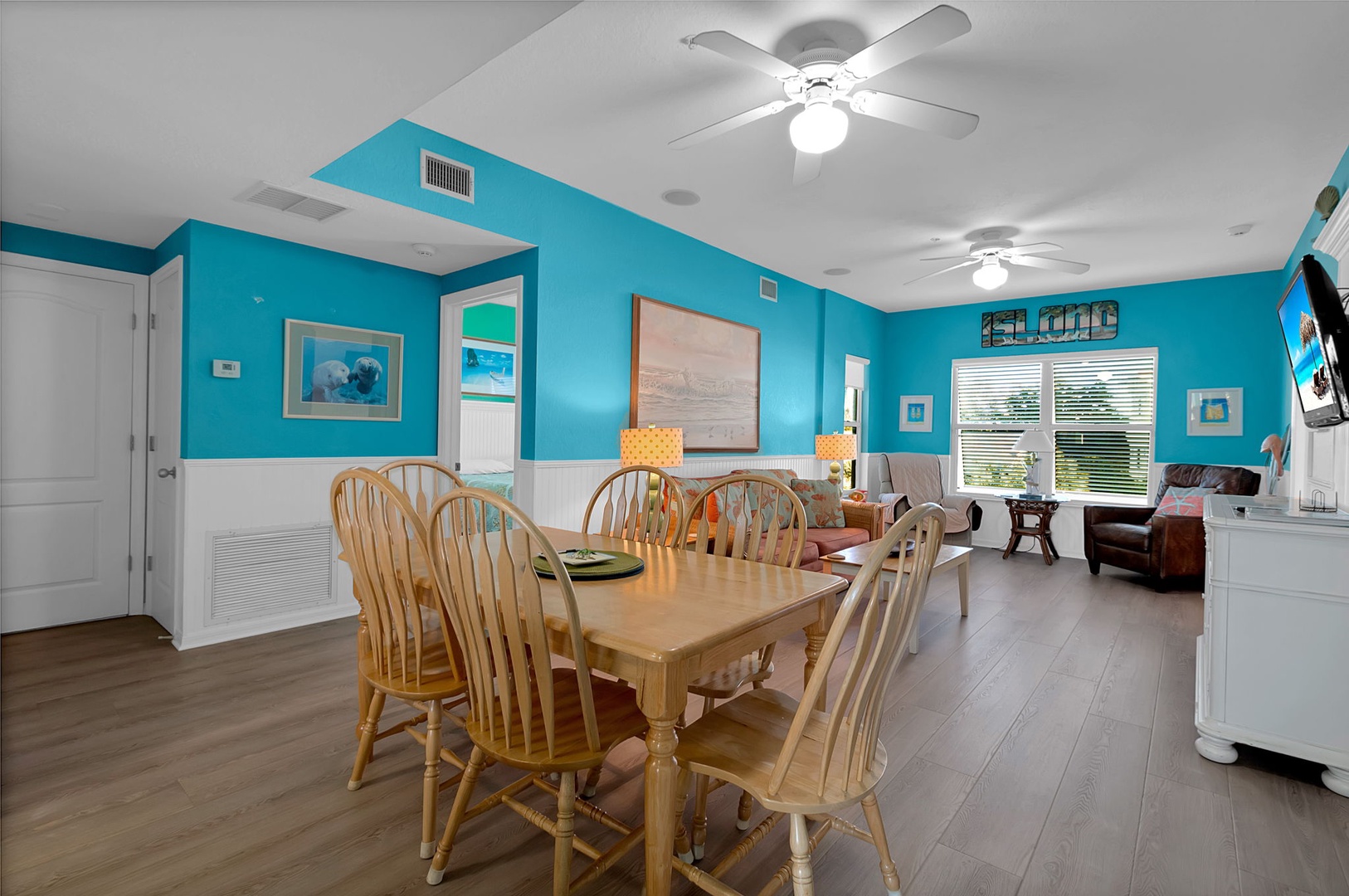 Step inside your bright coastal retreat with cheerful turquoise walls, a spacious dining table for family meals, and a cozy living area where you can unwind after beach adventures.