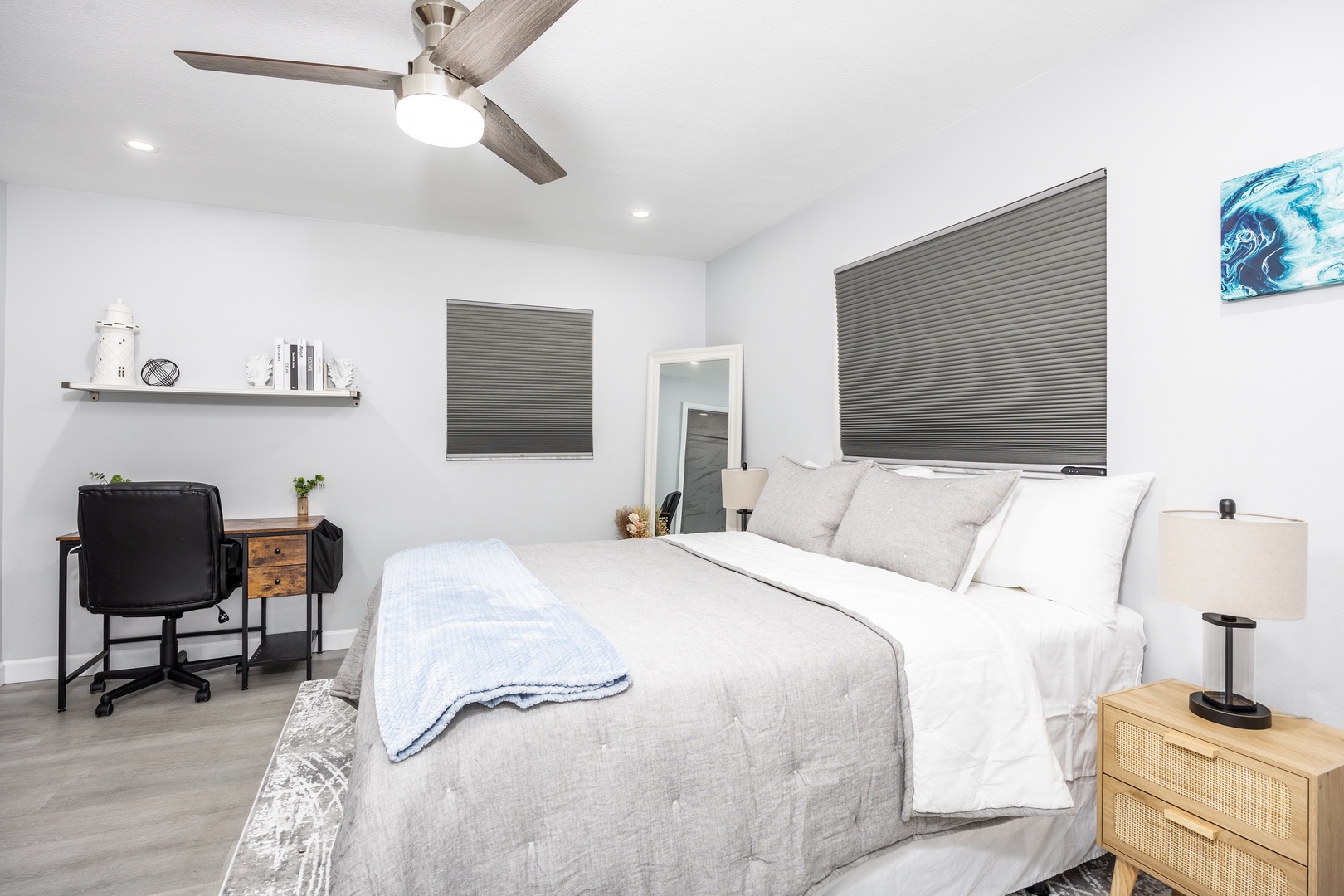 Relax in your serene bedroom with plush bedding, modern workspace, and cooling ceiling fan for perfect comfort.