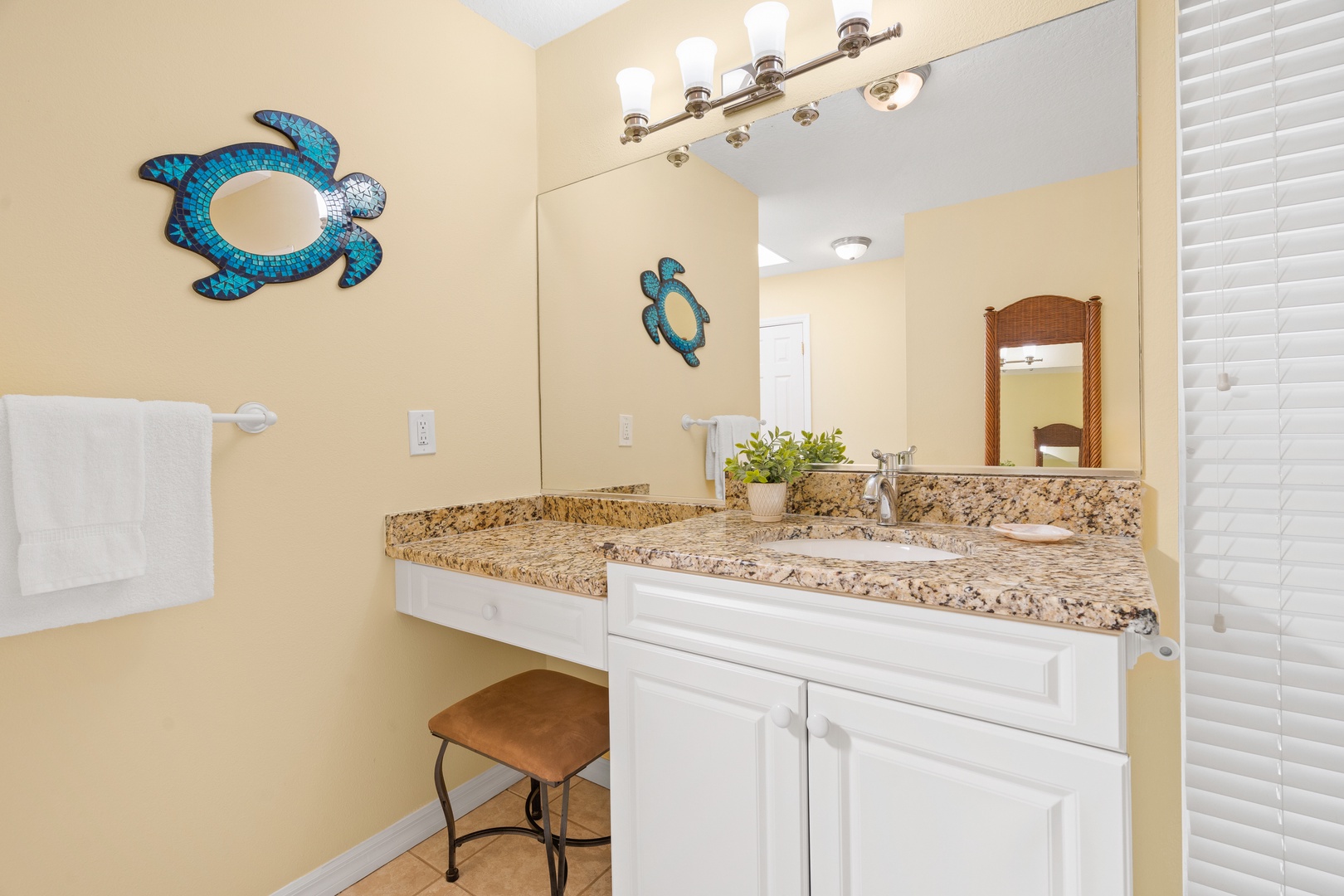 Pamper yourself in this bright bathroom featuring granite counters, a comfy vanity seat, and charming sea turtle decor.