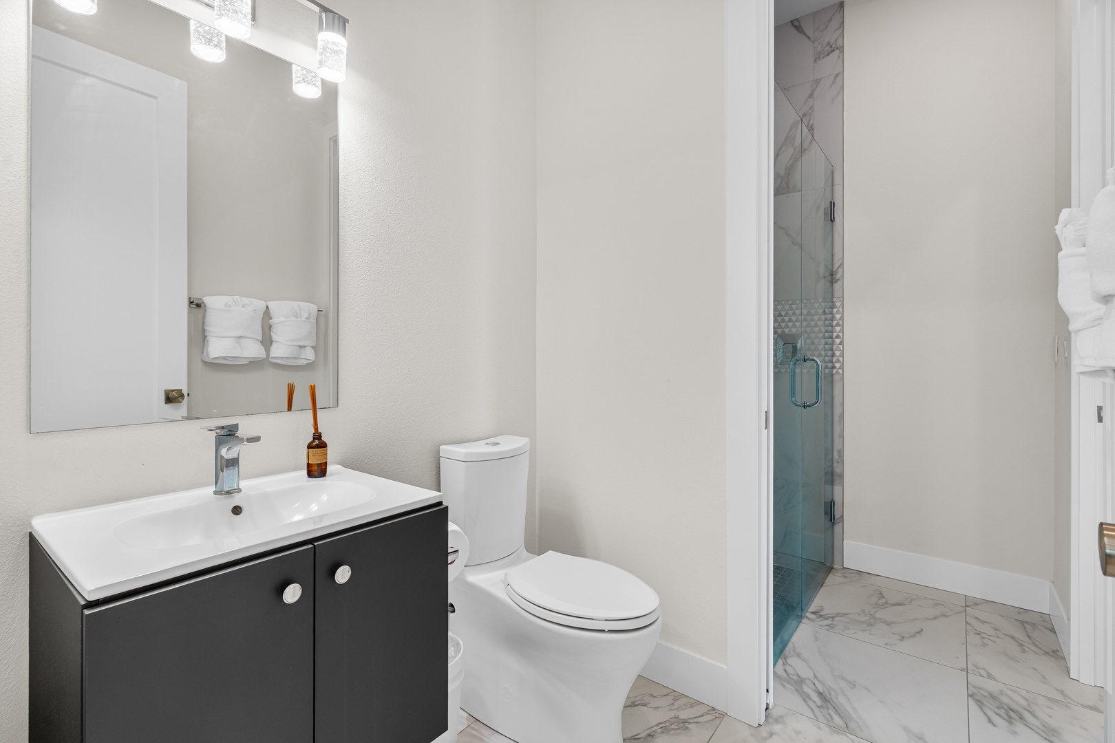 Step into your sleek, modern bathroom with stylish marble-look tile, a glass-enclosed shower, and fresh towels waiting for you. The crisp vanity and warm lighting create a space that's both functional and inviting.