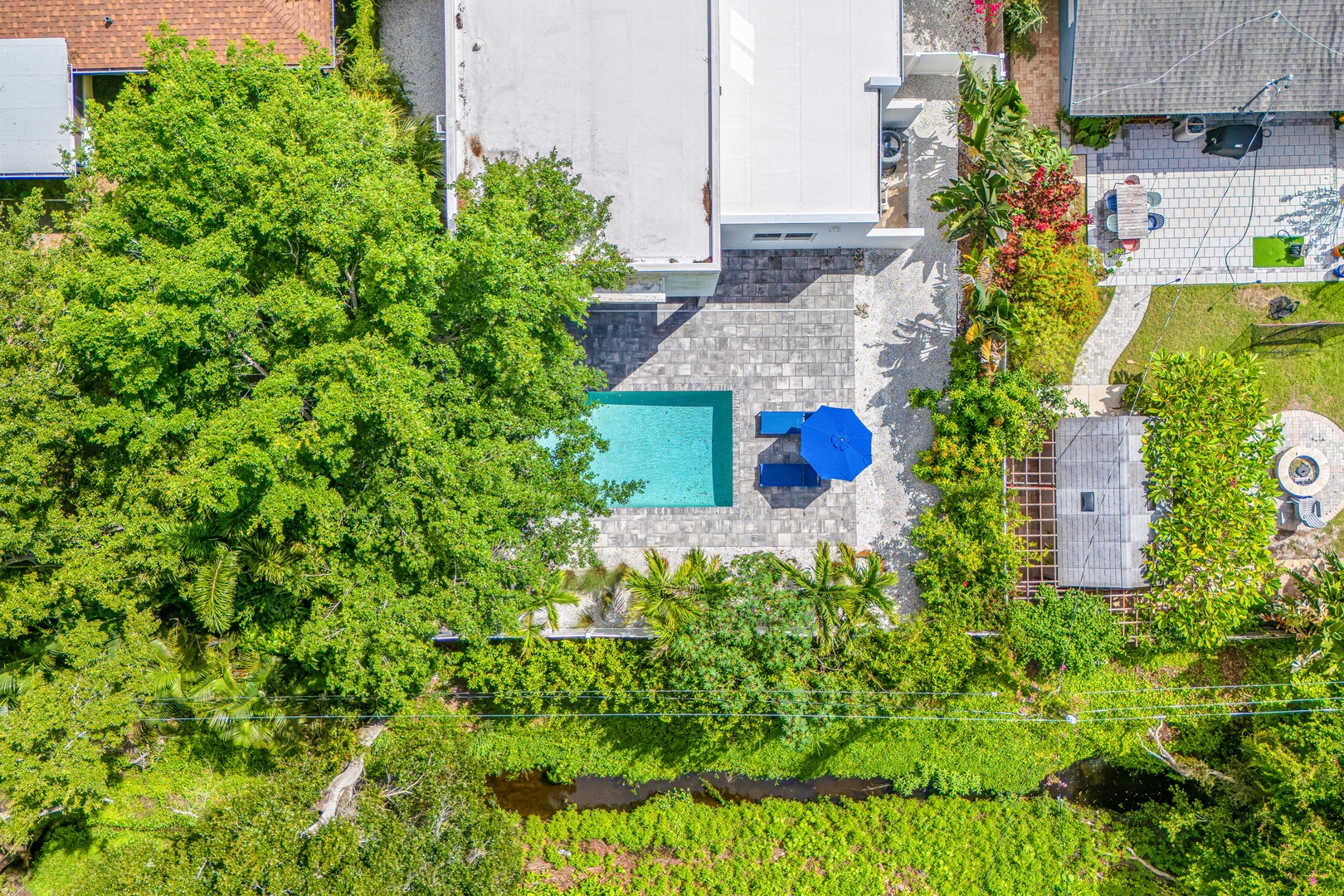 An aerial view showcases the property nestled among lush greenery with a sparkling pool and surrounding patio areas perfect for outdoor relaxation.