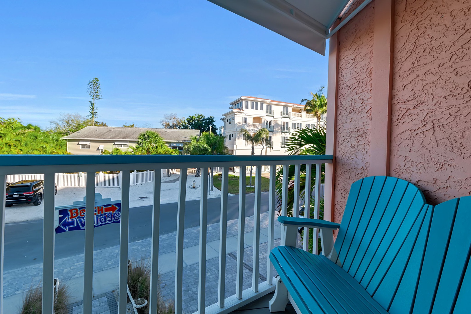 Bright blue Adirondack chair on your private balcony overlooking swaying palms and colorful coastal streets. Perfect for soaking up Florida sunshine and gentle breezes.