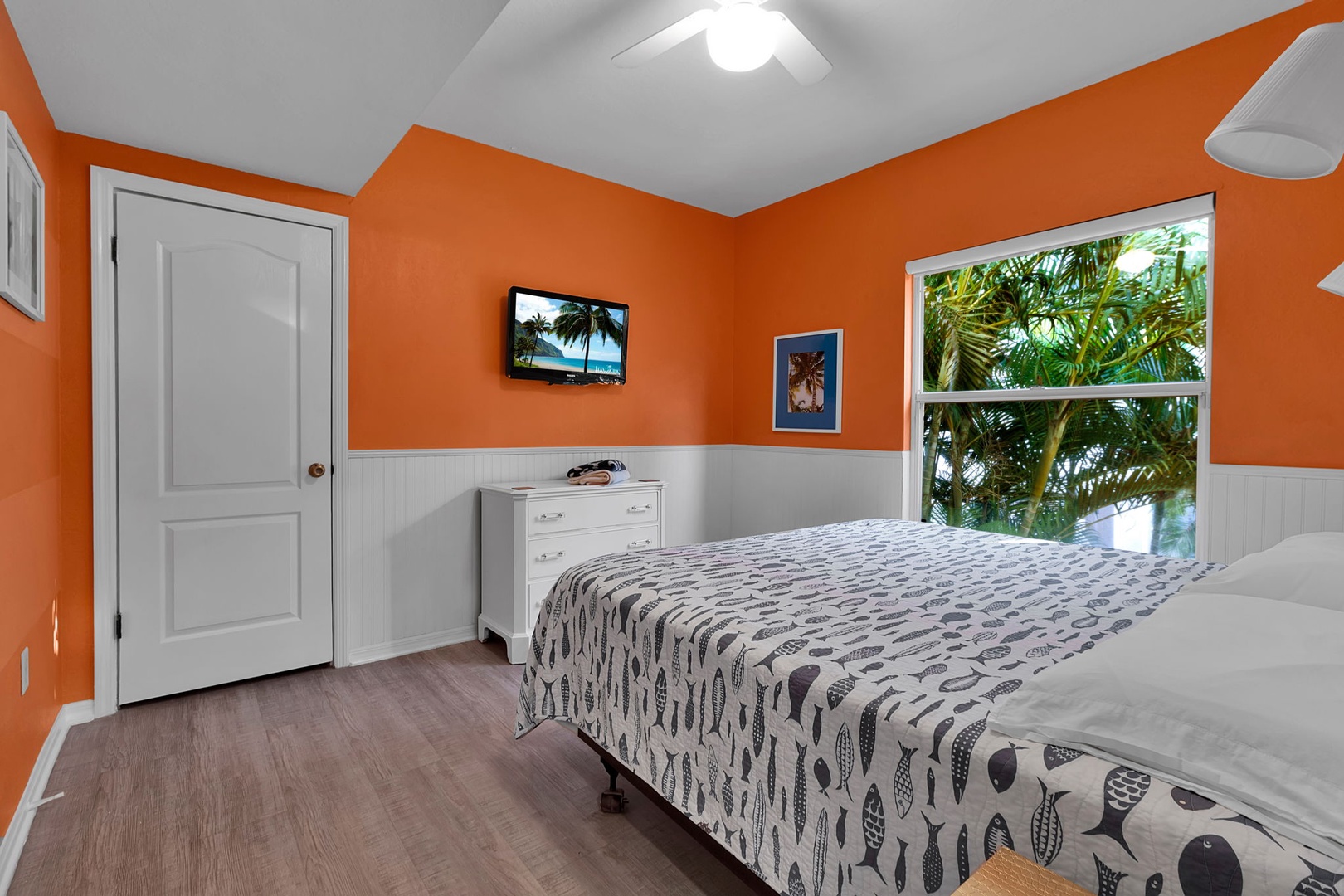 Your vibrant bedroom features cheerful orange walls and looks out onto lush tropical greenery through a large window, creating a bright and refreshing retreat.