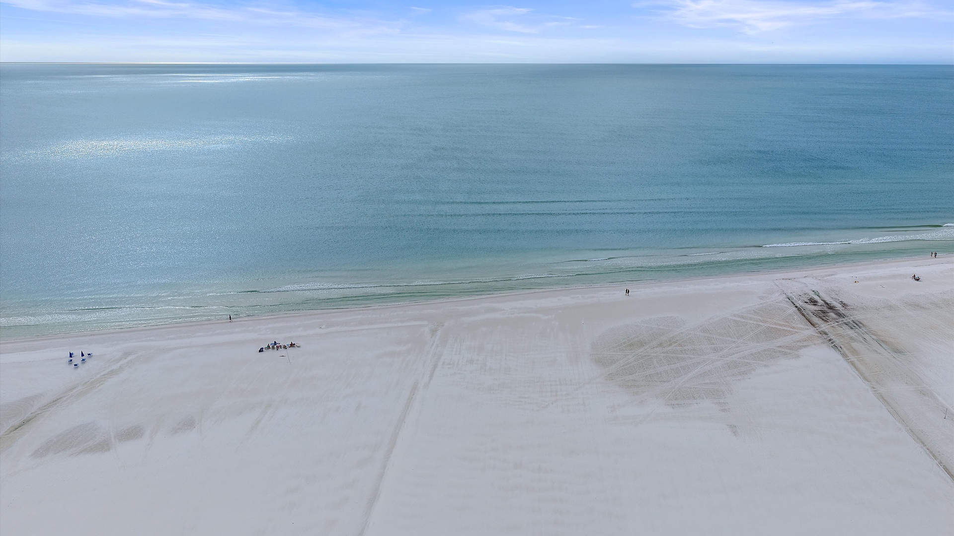Aerial view of pristine white sand beach stretching along crystal-clear turquoise waters under bright blue skies.