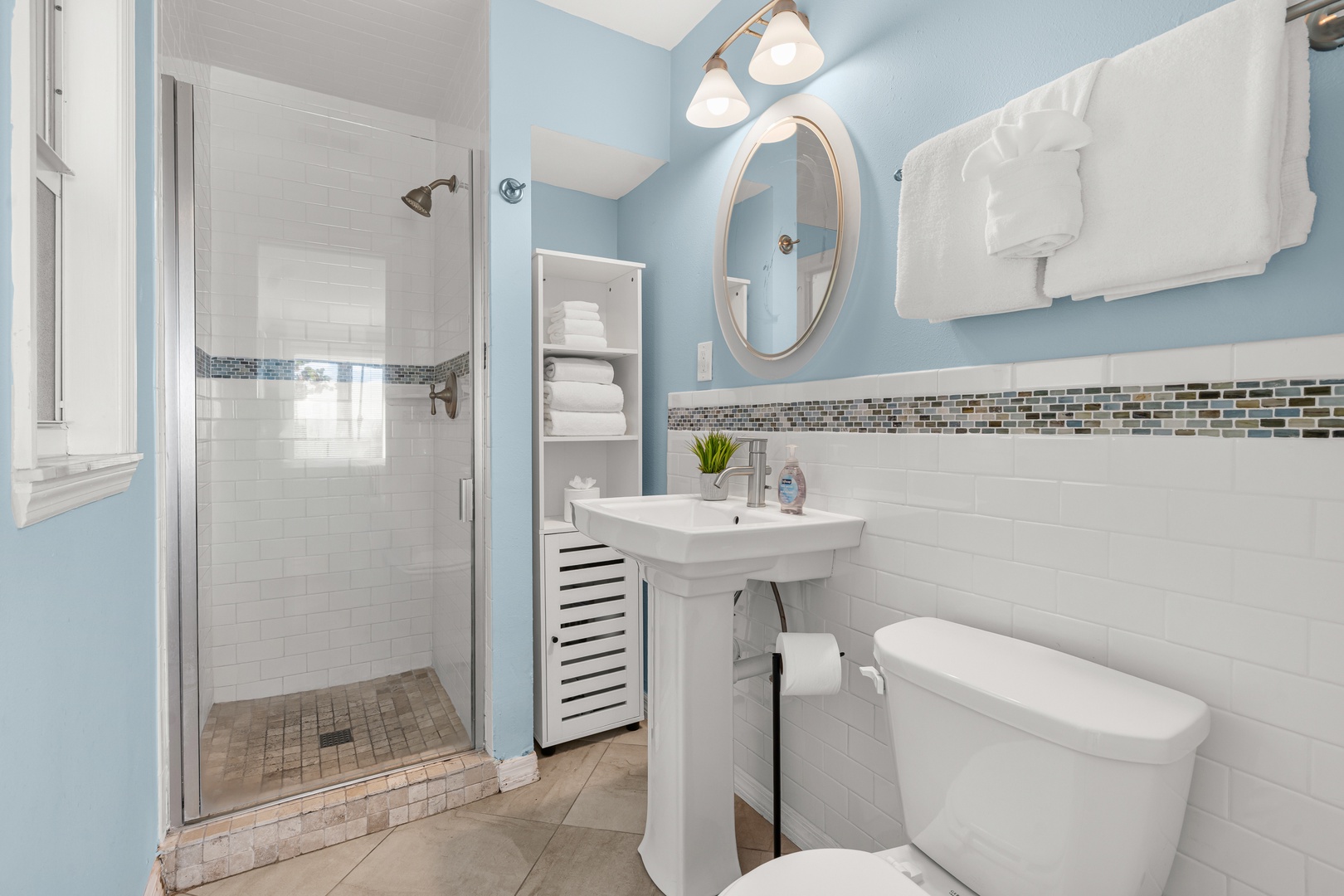 Refresh in your stylish bathroom featuring a spacious walk-in shower, pedestal sink, and soothing blue accents with elegant mosaic tile details.