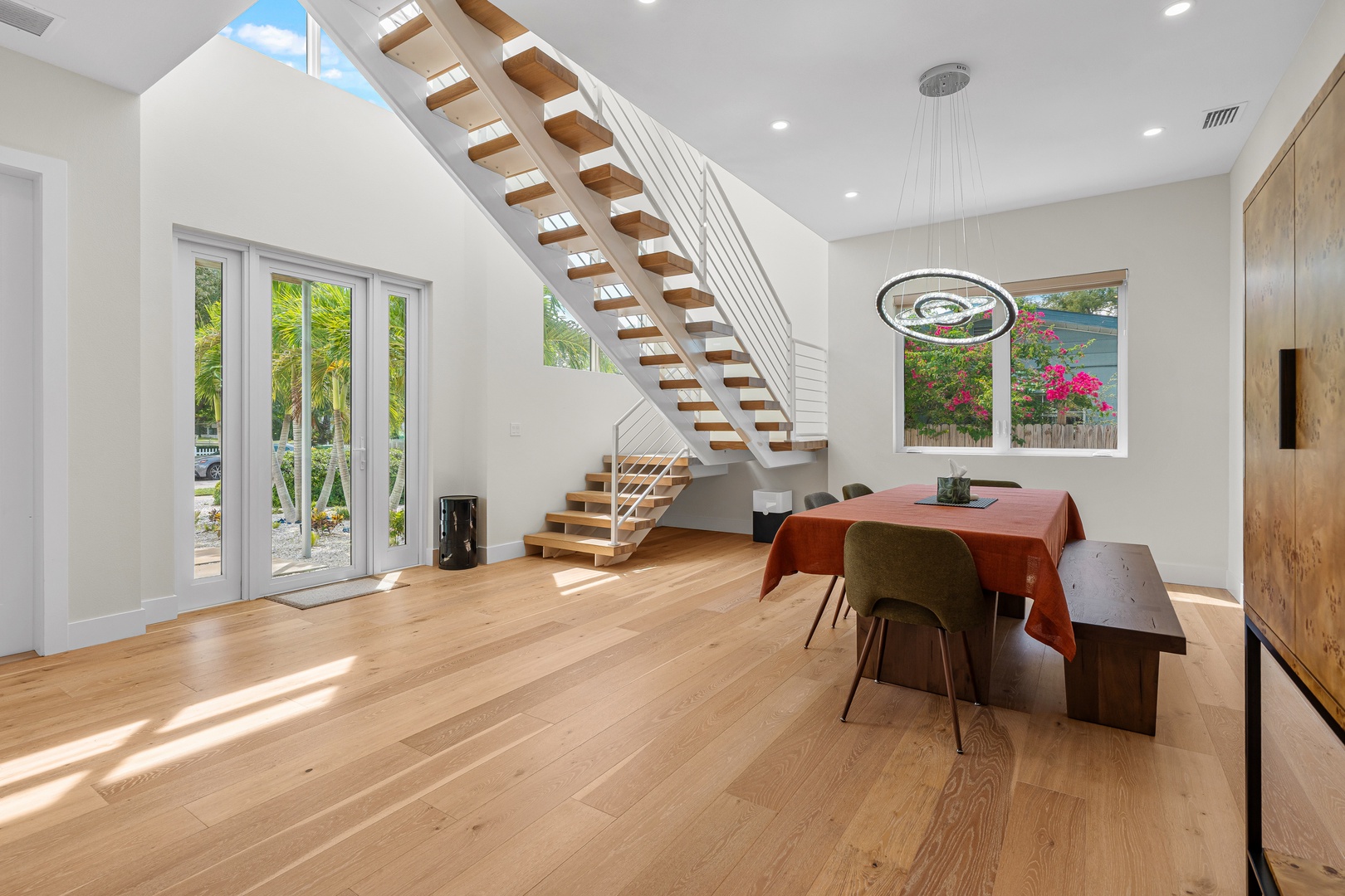 Gather around the dining table in this bright, airy space where sunlight pours in through skylights and windows framing garden views. The open layout and modern staircase invite you to make yourself at home.