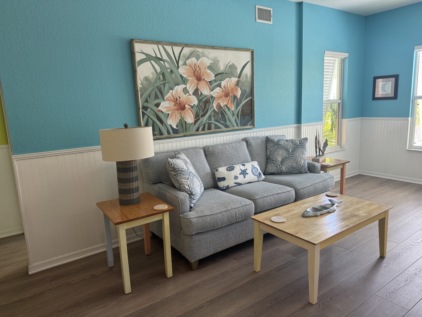 Step into your bright, coastal-inspired living room with soothing turquoise walls and coastal accents. Sink into the plush gray sofa and let the peaceful atmosphere wash over you as natural light streams through the windows.