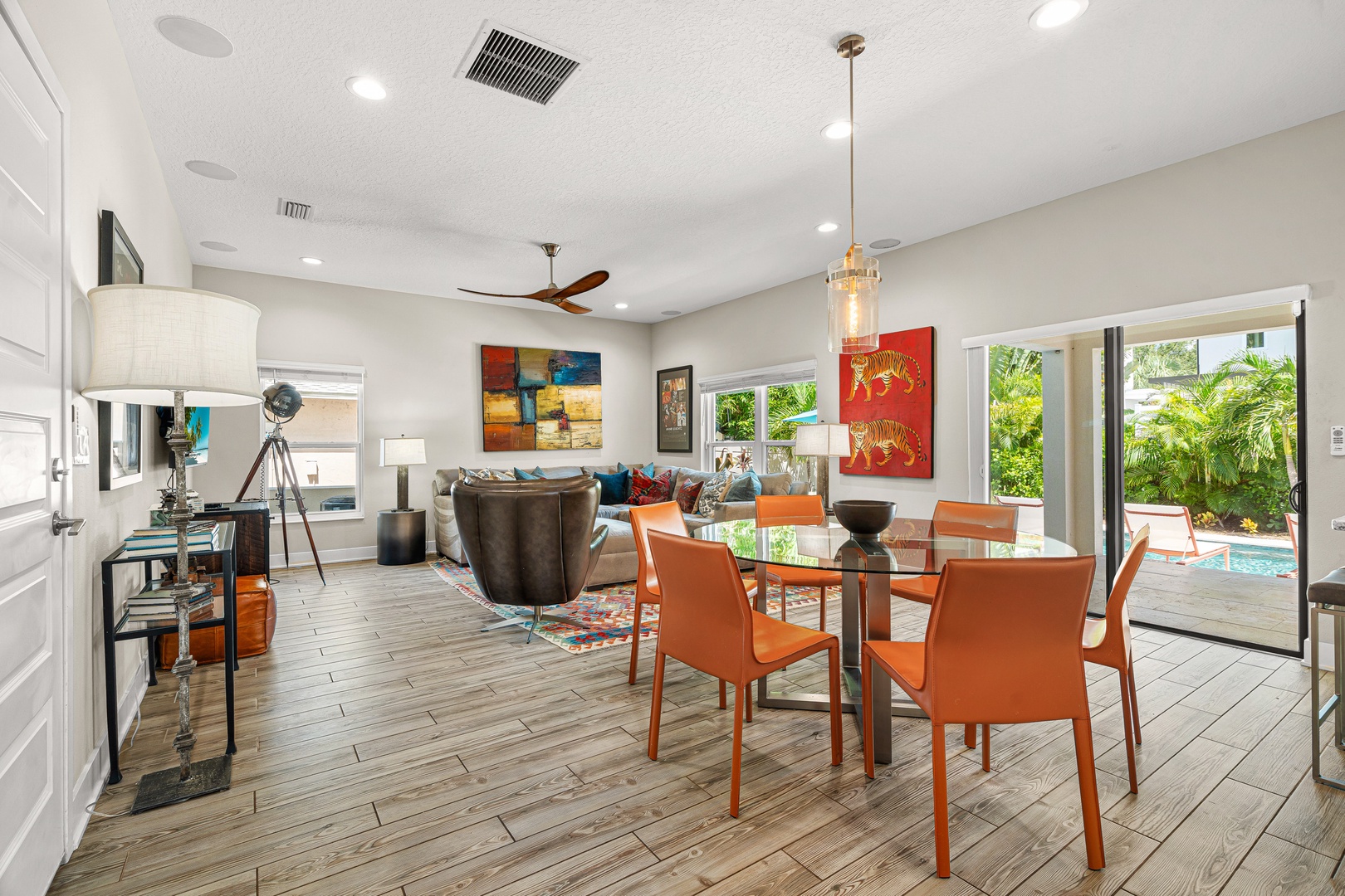 Vibrant orange accents and colorful artwork energize this open-concept living and dining space. Relax in the stylish lounge, dine at the modern table, and access your private pool oasis through glass doors framed by lush tropical palms.