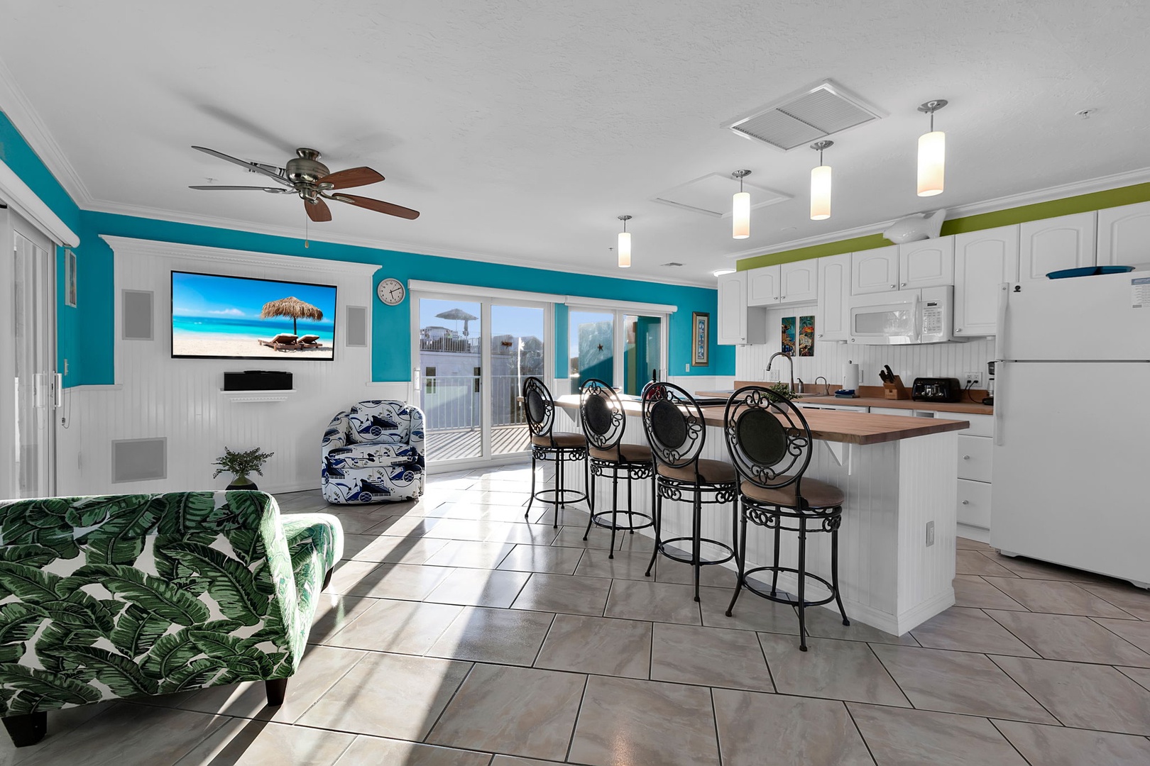Sink into the palm-printed sofa and soak in the vibrant coastal vibe, where the kitchen island invites gathering and bright natural light pours through sliding doors.