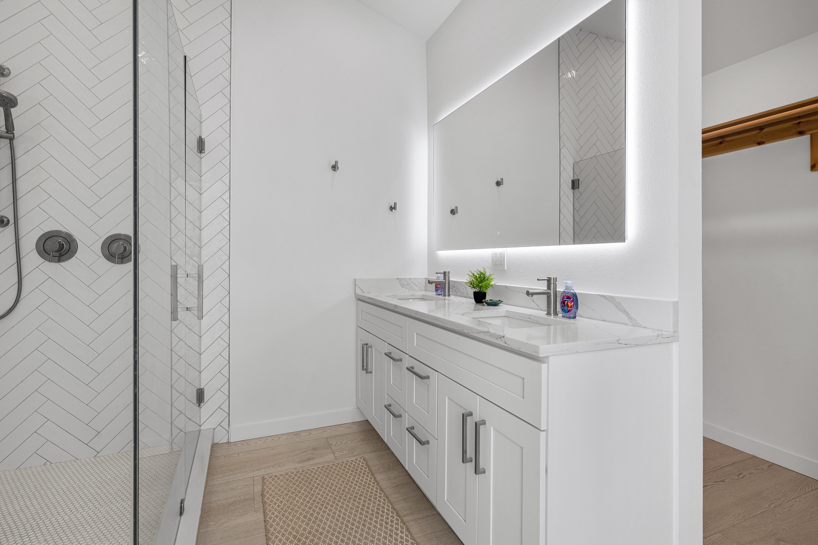 Step into your bright, modern bathroom with dual vanities, a walk-in herringbone-tiled shower, and a stylish backlit mirror to start your mornings refreshed.