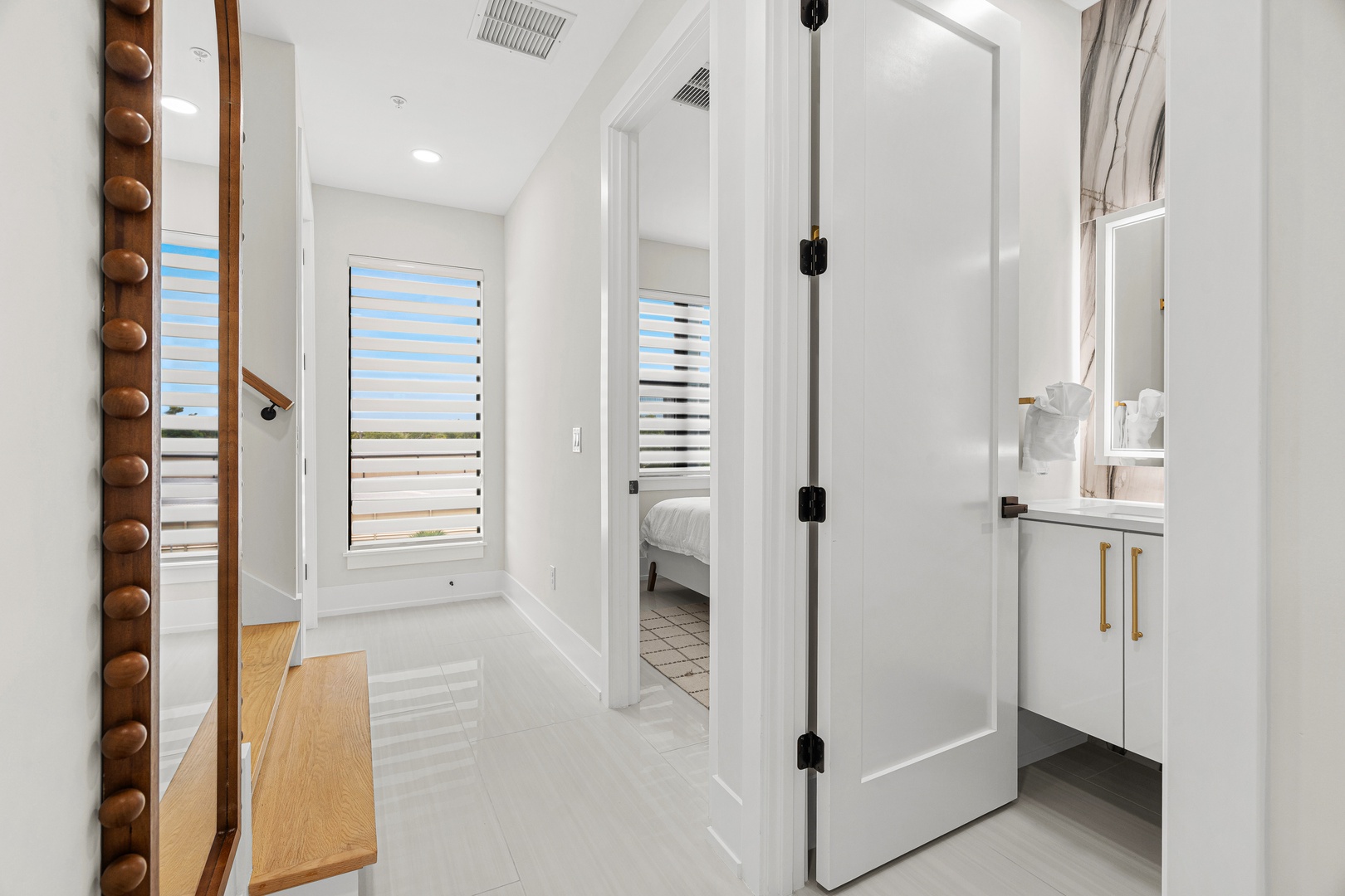 Light-filled hallway connects your private bedroom and modern bathroom, with crisp white walls and warm wood accents creating an inviting coastal retreat.