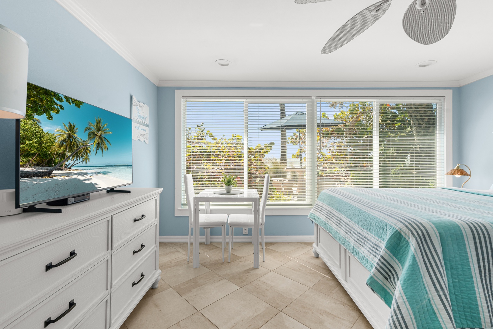 Your bright bedroom features calming blue walls, tropical art, and windows overlooking leafy surroundings.