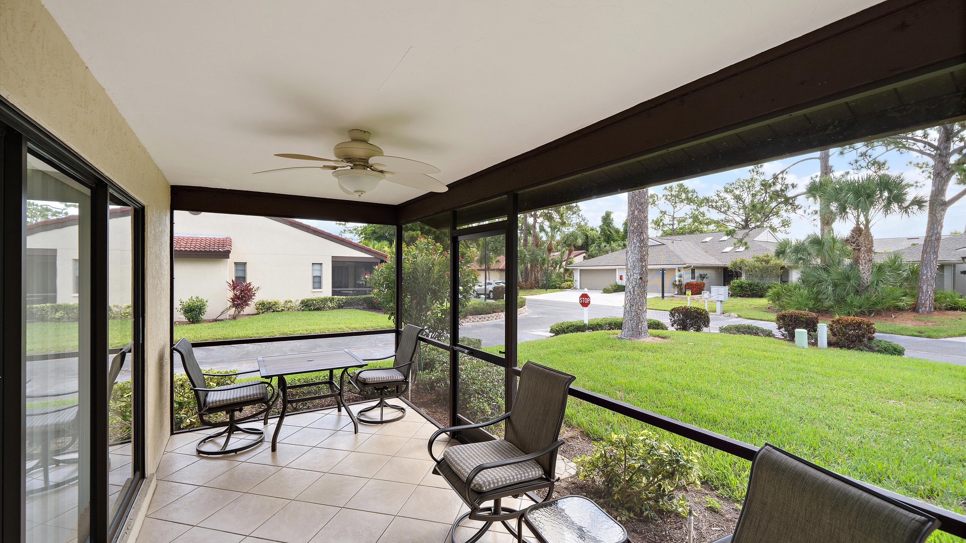 A screened patio overlooks a residential neighborhood with green lawns and palm trees, offering a peaceful setting for outdoor relaxation near the property entrance.