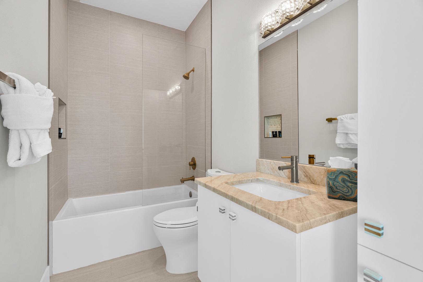 Your bathroom features a modern tub-shower combo, plush towels, and a marble-topped vanity with gold fixtures. Relax and refresh in this bright, elegantly tiled space.