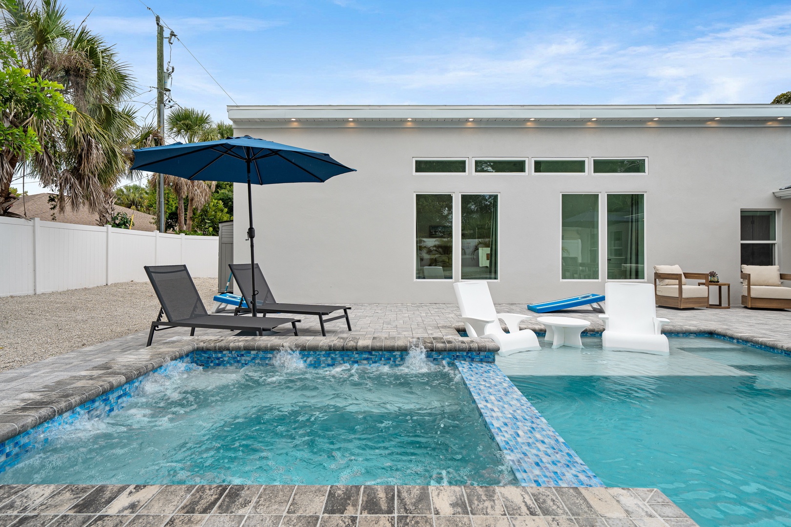 Lounge by your private pool with spa jets, shaded seating, and direct access to modern indoor-outdoor living spaces surrounded by tropical palms.