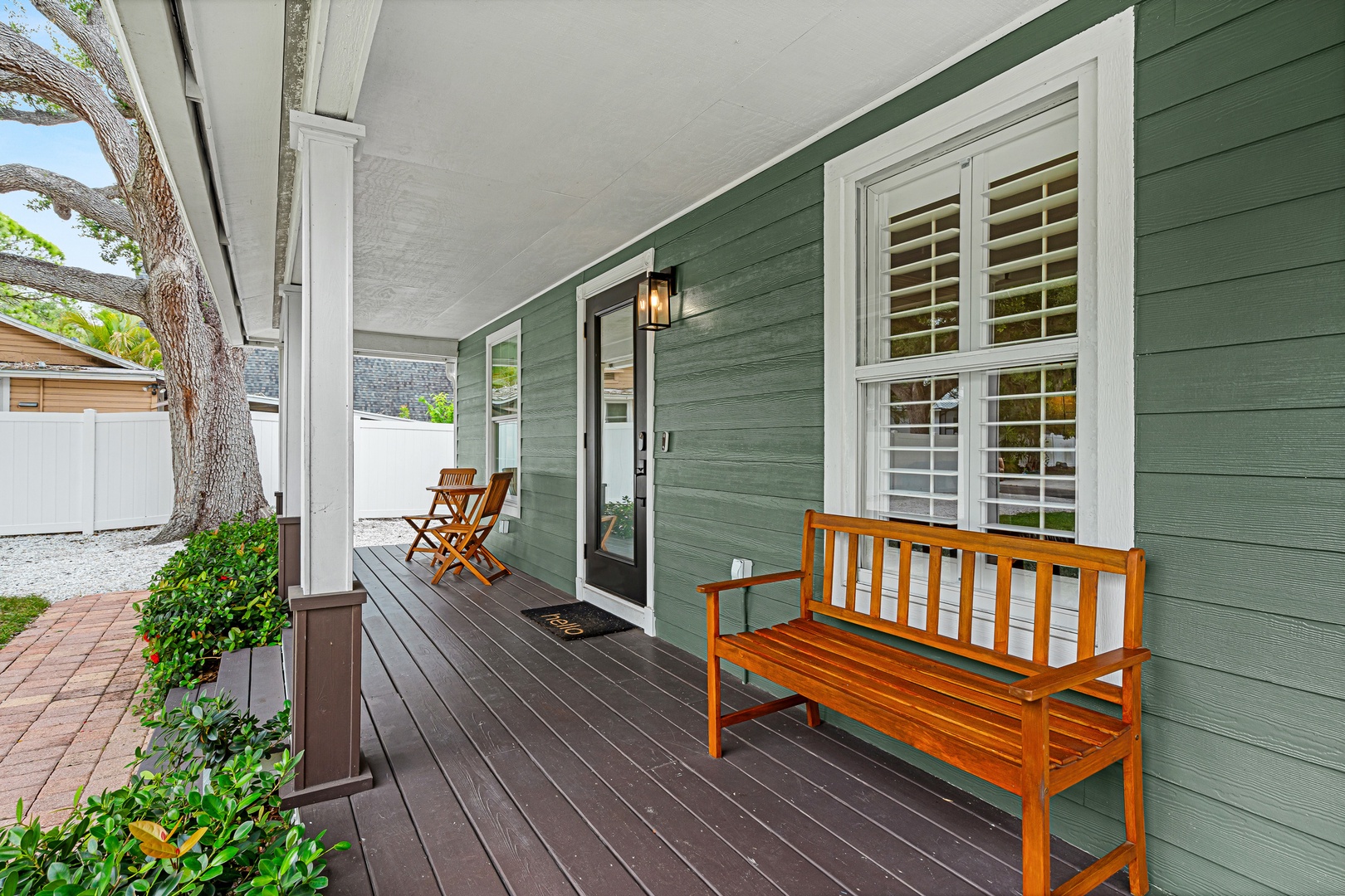 The welcoming front porch offers a peaceful spot to enjoy your morning coffee on the wooden bench, surrounded by lush greenery and charming details.