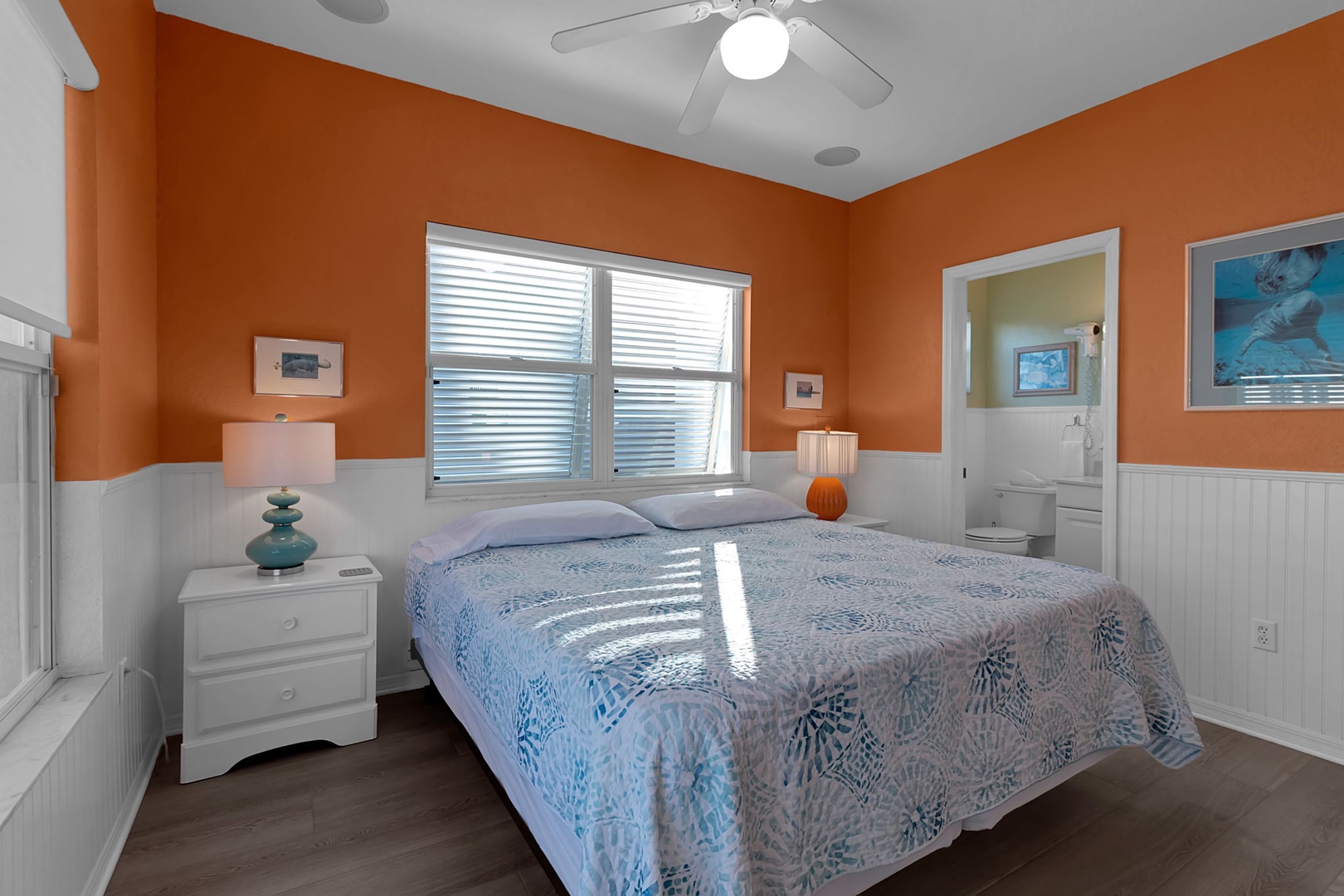 Step into your serene bedroom retreat, where warm orange walls meet crisp white accents and gentle sunlight filters through the windows. You'll rest peacefully in the comfortable bed, while your private bathroom awaits just steps away.