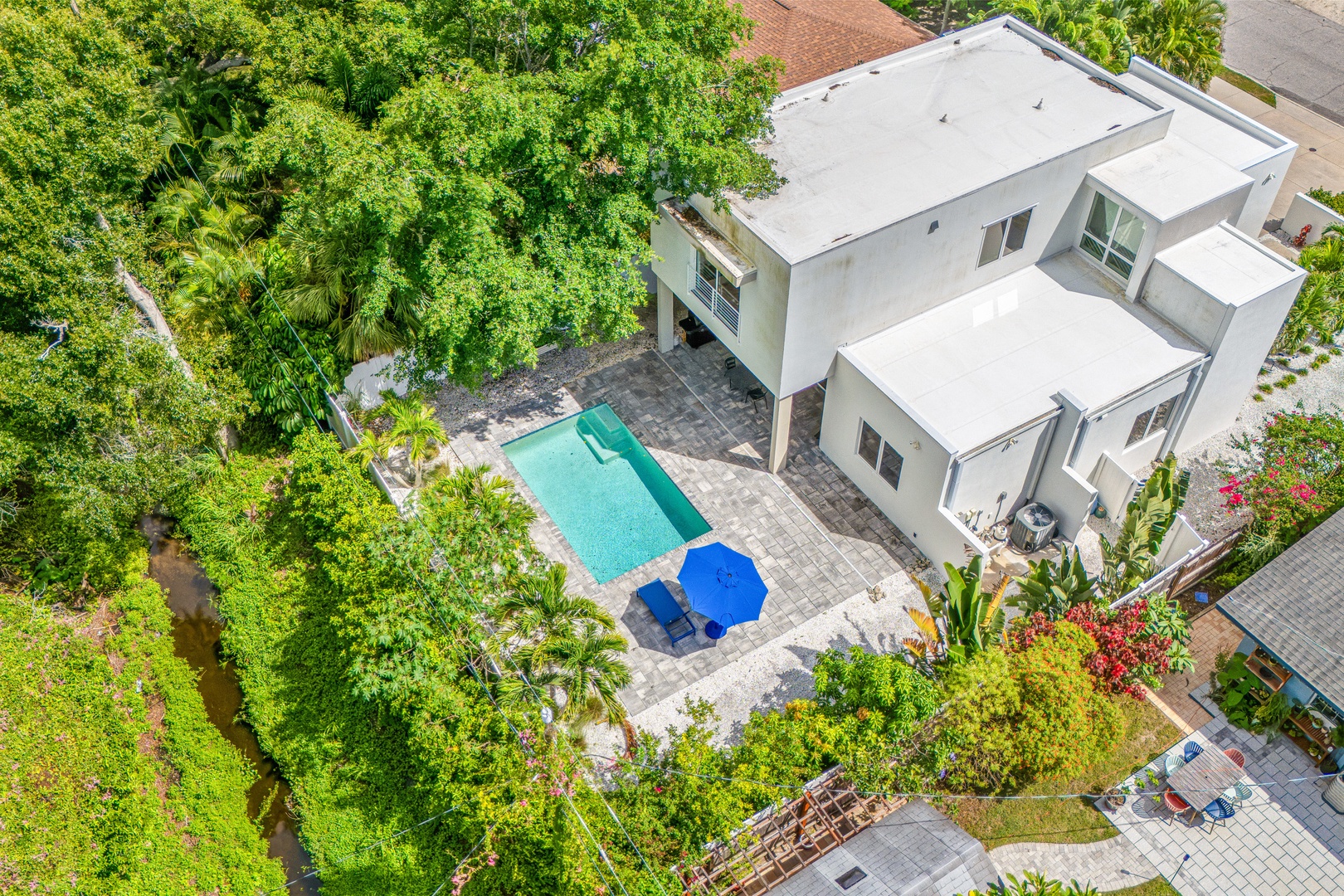 Aerial view of this modern vacation home featuring a private pool, spacious patio, and lush tropical landscaping nestled in a quiet residential neighborhood.