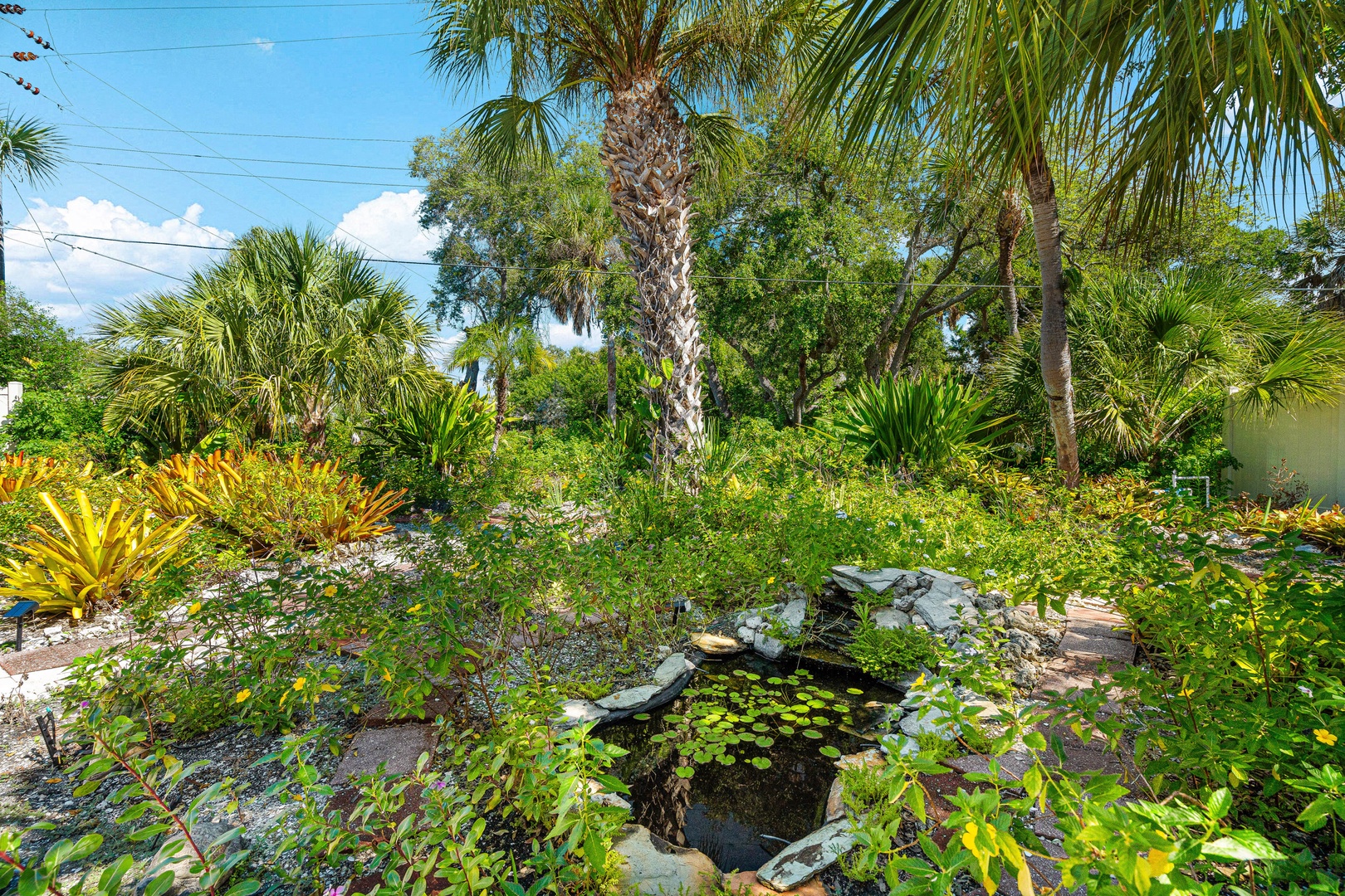 A lush tropical garden featuring palm trees, vibrant greenery, and a tranquil koi pond creates a peaceful natural setting for the property.