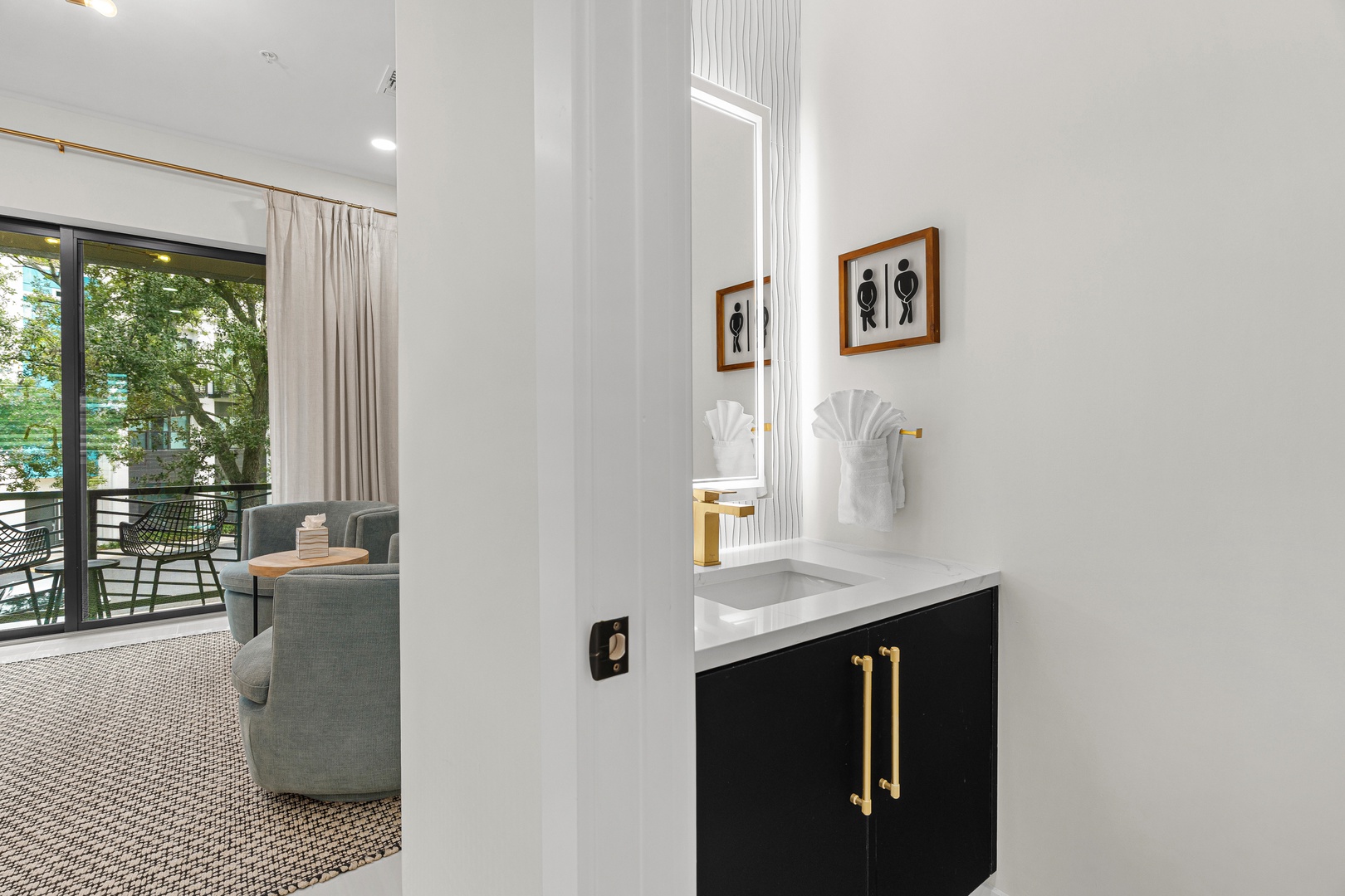Fresh towels await you in this sleek bathroom, where modern black-and-white design pairs with stylish gold accents. Beyond, your living space opens to a peaceful green view, blending comfort with nature.