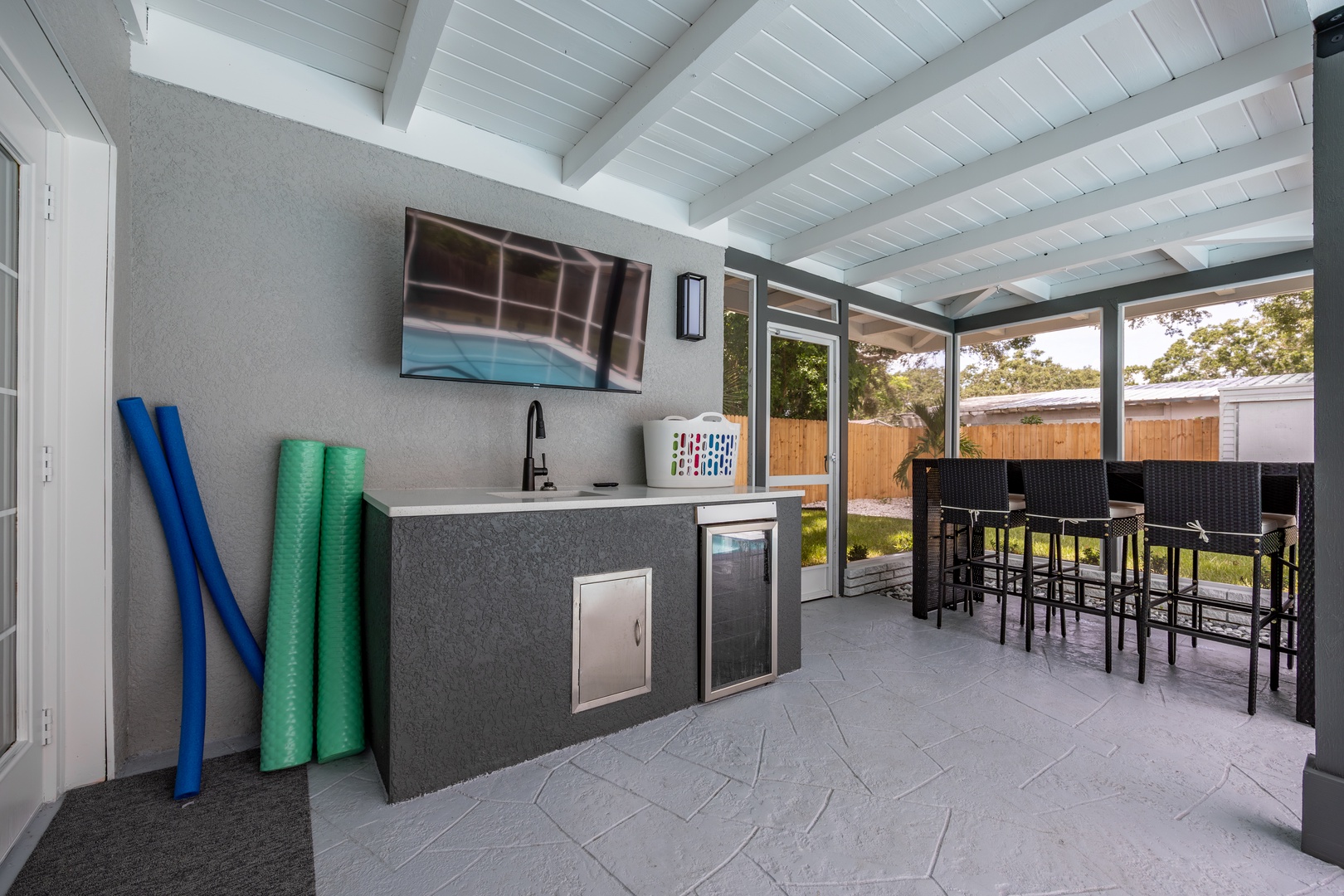 Your covered outdoor kitchen features everything for poolside entertaining—sink, mini fridge, and bar seating under stylish beamed ceilings.