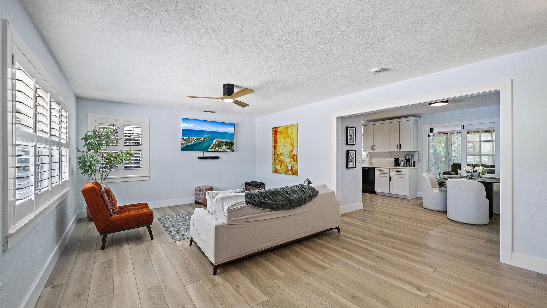 Your open-concept living space flows seamlessly from lounge to kitchen, bathed in natural light through plantation shutters. Relax on the sofa, enjoy the ceiling fan's gentle breeze, and settle in for a truly comfortable stay.