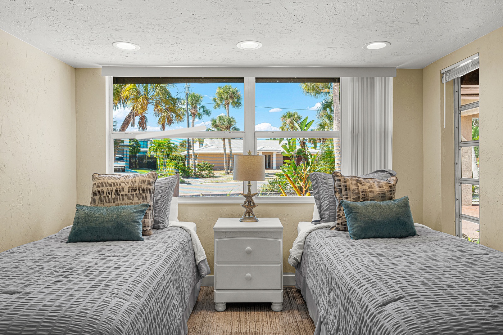 Twin beds dressed in soft coastal linens frame your view of swaying palms and sunny blue skies. Wake up refreshed in this light-filled bedroom where tropical scenery greets you every morning.