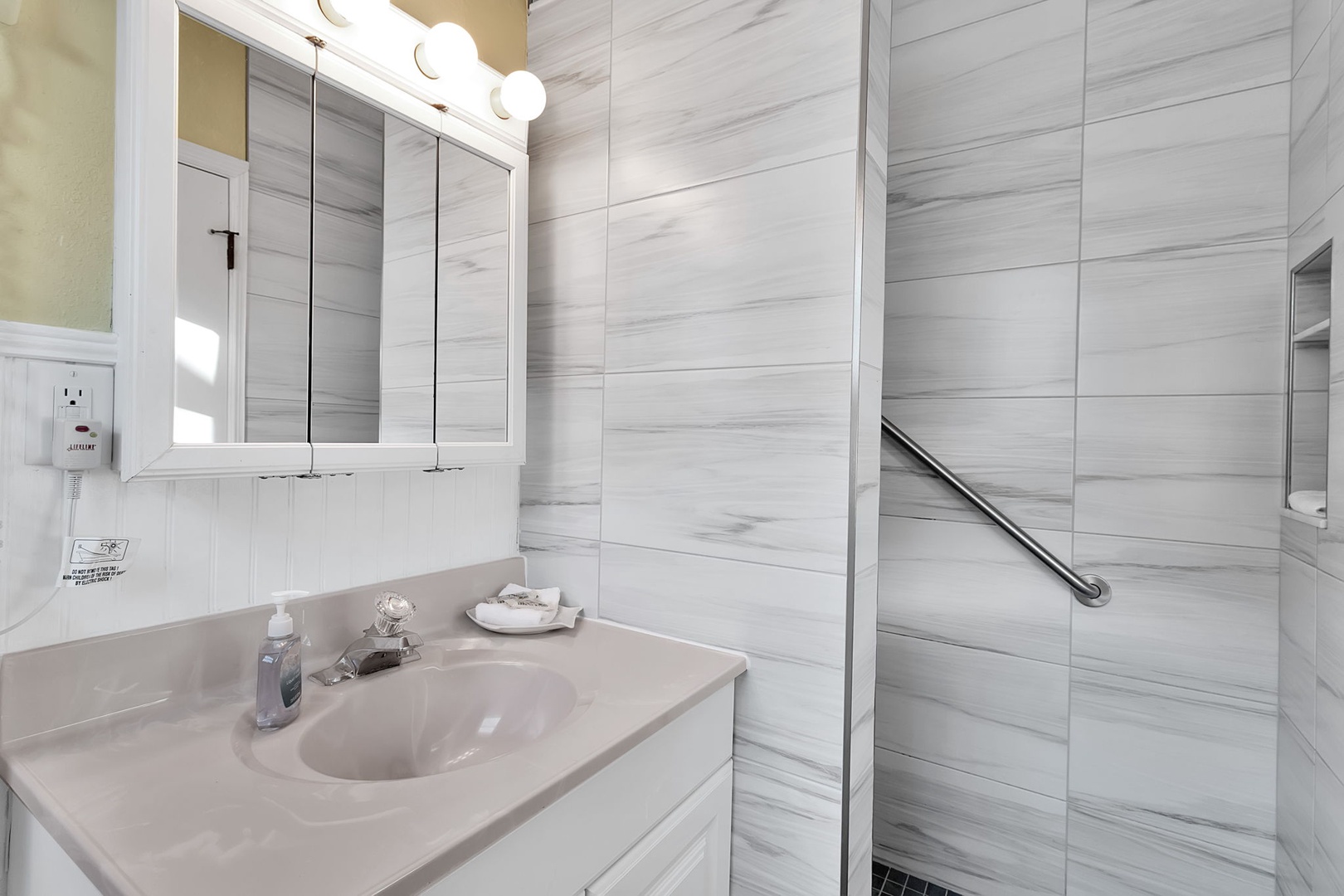 Your private bathroom features a walk-in shower with elegant marble-style tiling, thoughtful grab bars for safety, and a vanity stocked with fresh towels and essentials to help you feel right at home.