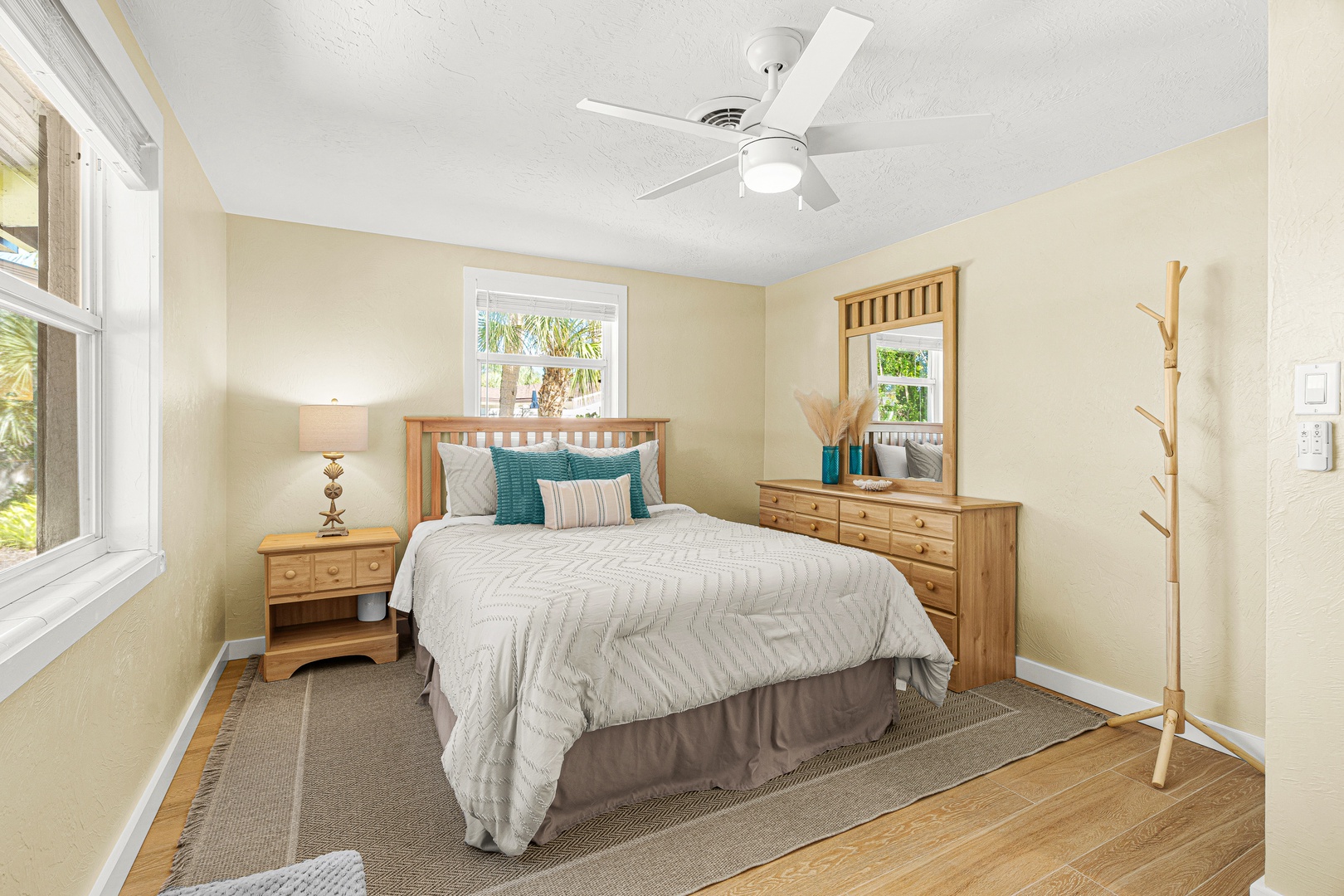 Drift off in your serene bedroom with soft coastal accents, natural wood finishes, and a gentle ceiling fan above. Palm trees peek through the windows, hinting at the tropical escape waiting just outside.