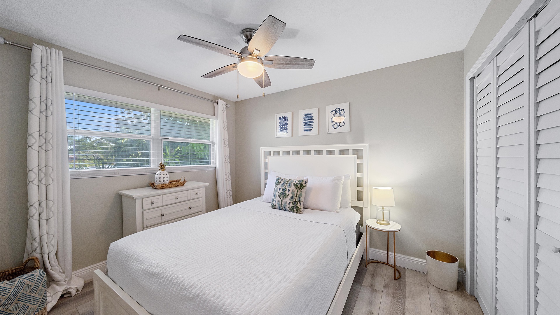 Sink into crisp white linens and let the ceiling fan's gentle breeze lull you to sleep. Natural light filters through the windows, framing your serene retreat.
