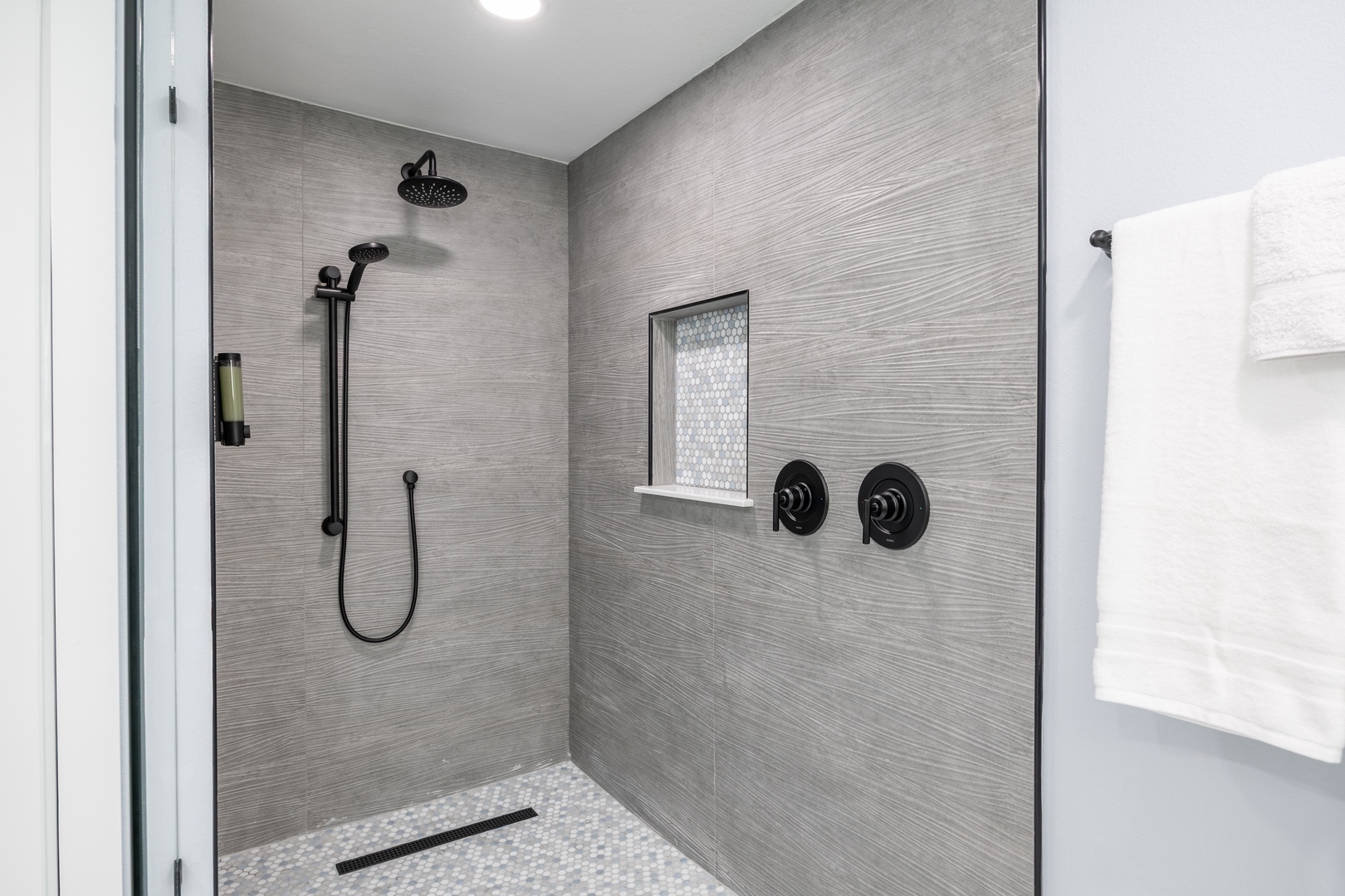 Step into your private spa-inspired shower featuring elegant gray tiles, dual rainfall heads, and luxurious amenities for ultimate relaxation.