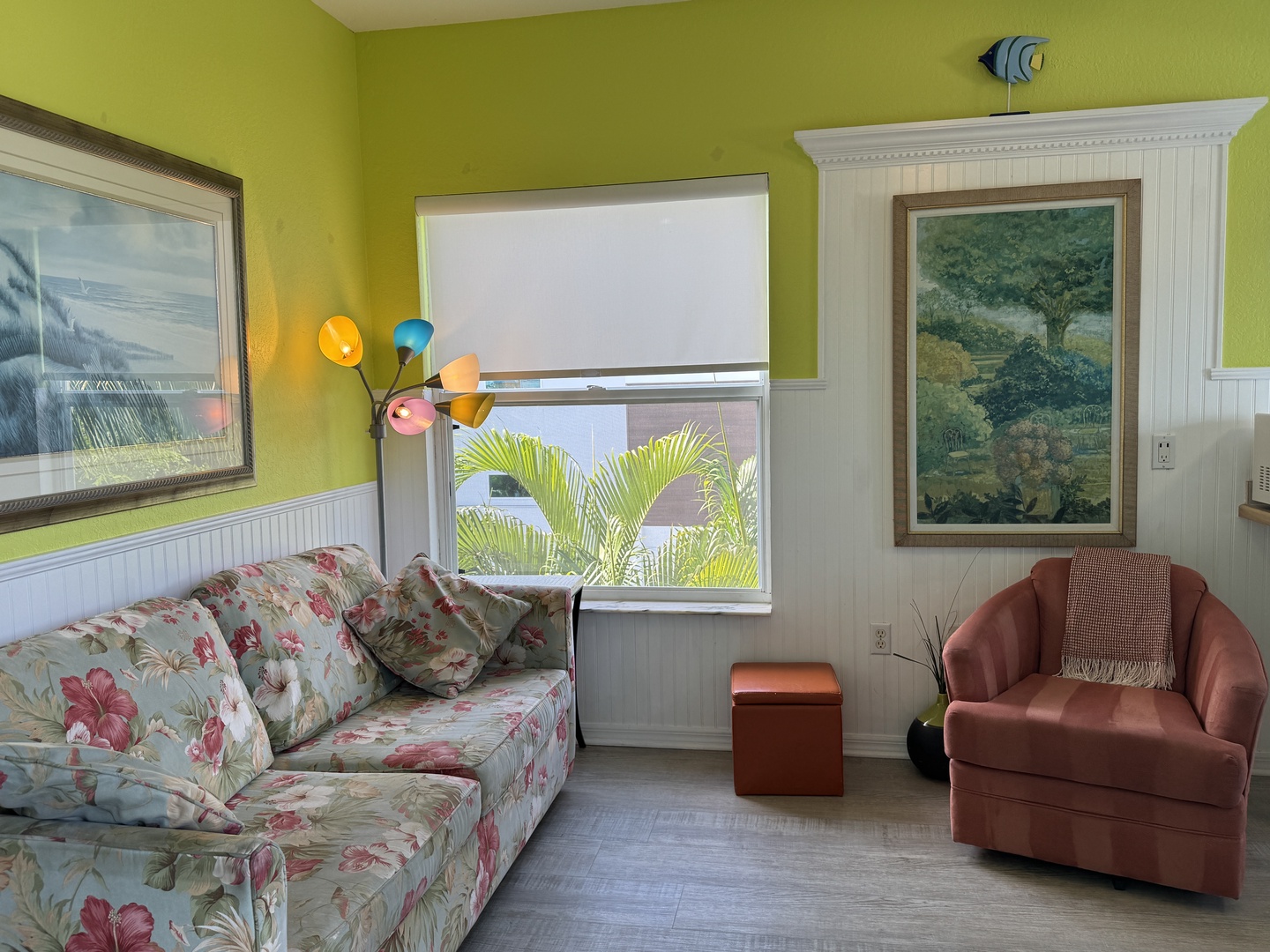 Bright chartreuse walls warm this cozy living area, where you can sink into floral-print seating or curl up in the terracotta chair with your favorite book. Natural light pours through the window framing palm fronds outside.