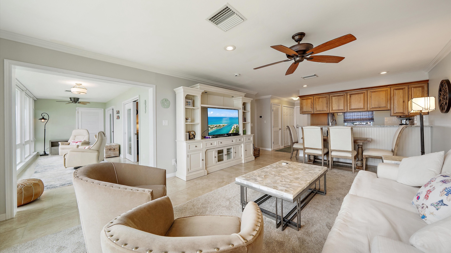 A spacious living area with a large television, inviting seating, and an adjoining dining space. Cream upholstery and soft neutral finishes keep the room bright, comfortable, and easy to enjoy.
