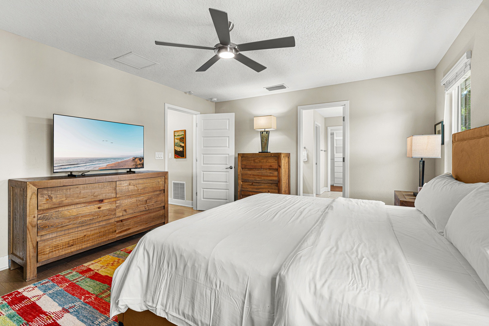 Drift off to sleep in your cozy bedroom with crisp white linens, warm wood furnishings, and gentle overhead fan. Two private doorways offer peaceful retreat and convenience.