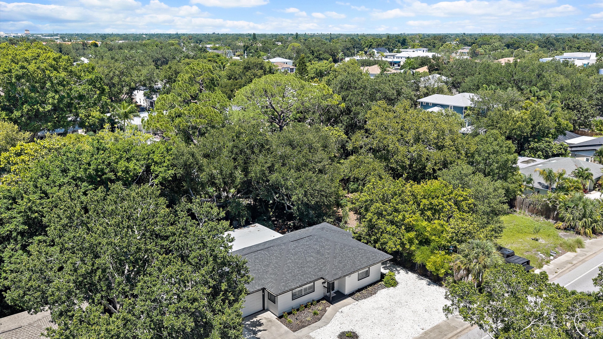 Aerial view of the property nestled in a lush, tree-lined neighborhood with ample green space and a peaceful residential setting.