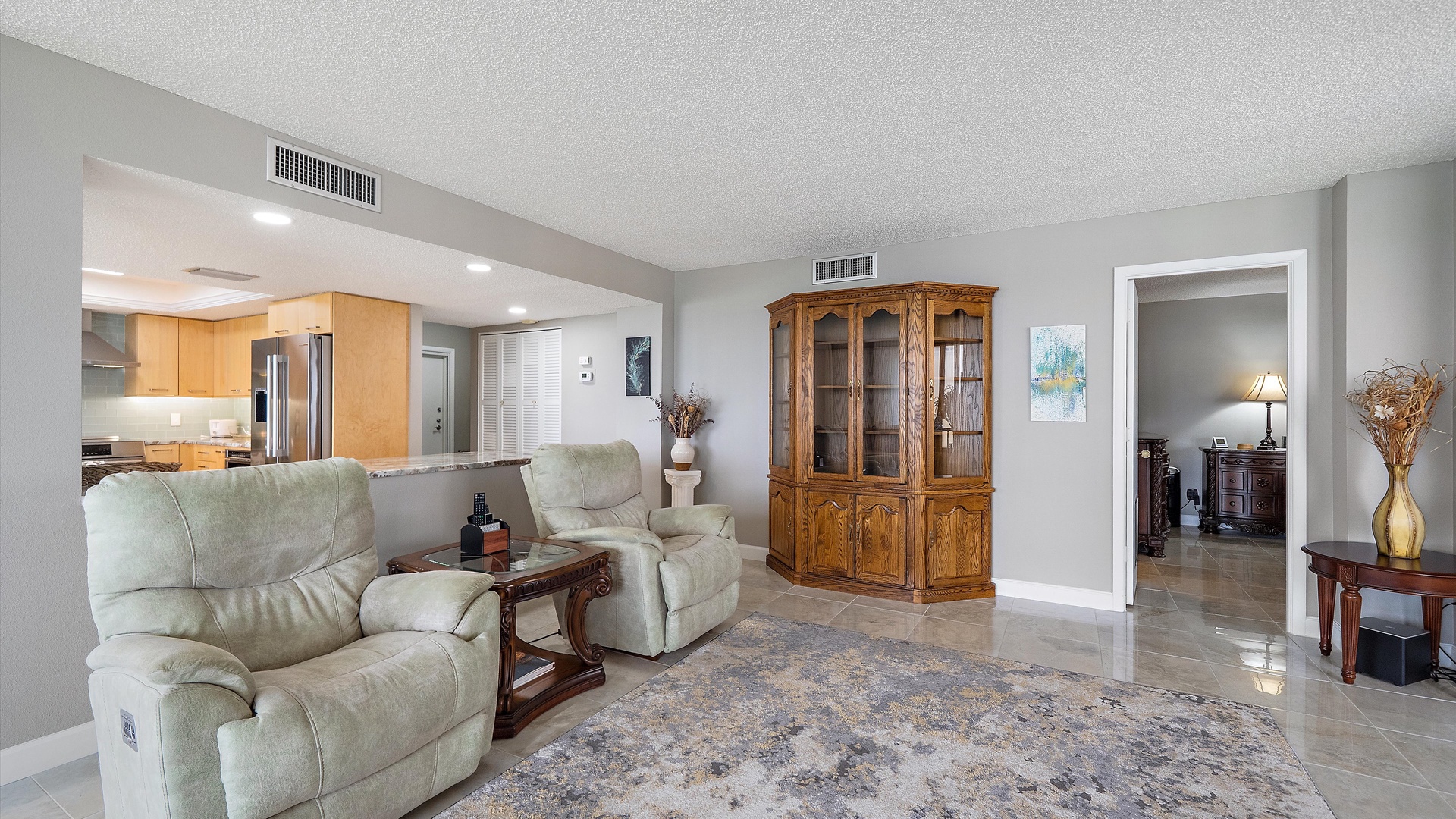 Relax in your spacious living room featuring plush recliners, elegant wood furnishings, and an open-concept design that flows seamlessly into the modern kitchen.