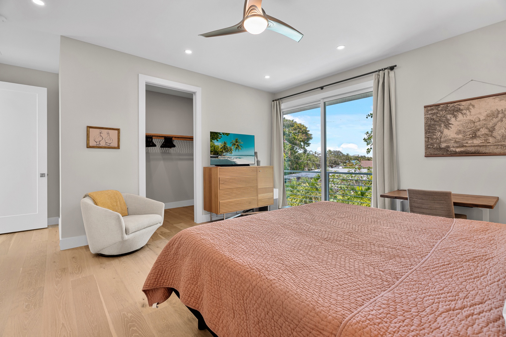 Wake up in your serene bedroom where natural light pours through large windows, revealing lush green views beyond. Sink into the plush bed, curl up in the cozy armchair, and let the modern ceiling fan keep you cool on warm mornings.