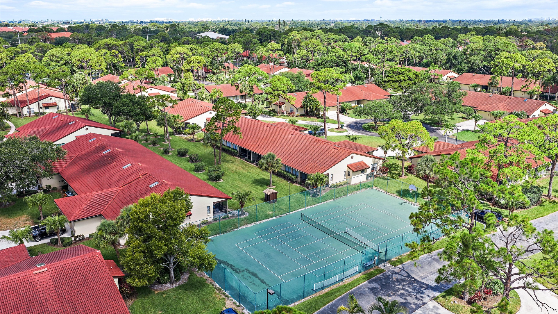 Aerial view of a lush residential community with red-tiled roofs, tennis courts, and abundant green spaces forming the scenic surroundings of the property.