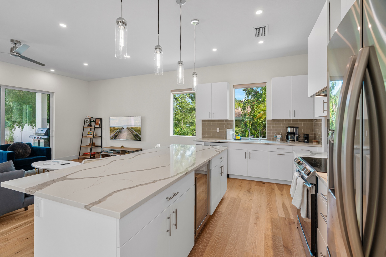 Sleek modern kitchen featuring white cabinetry, stainless appliances, and a spacious island. Natural light streams through oversized windows, creating a bright and inviting space.