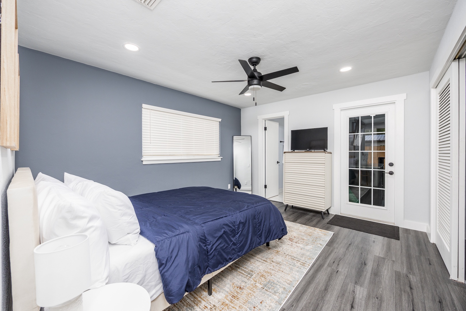 Relax in your serene bedroom with crisp white linens and calming blue accents. The ceiling fan keeps you cool while French doors open to outdoor space.