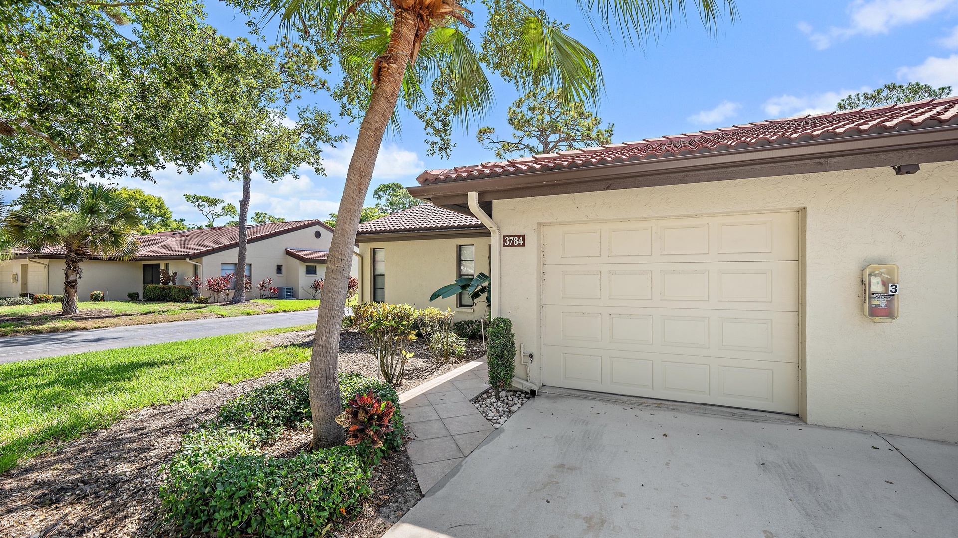 Single-level villa with private driveway and garage in a quiet, manicured neighborhood. Mediterranean-style architecture with palm trees and tropical landscaping surrounds this peaceful residential retreat.