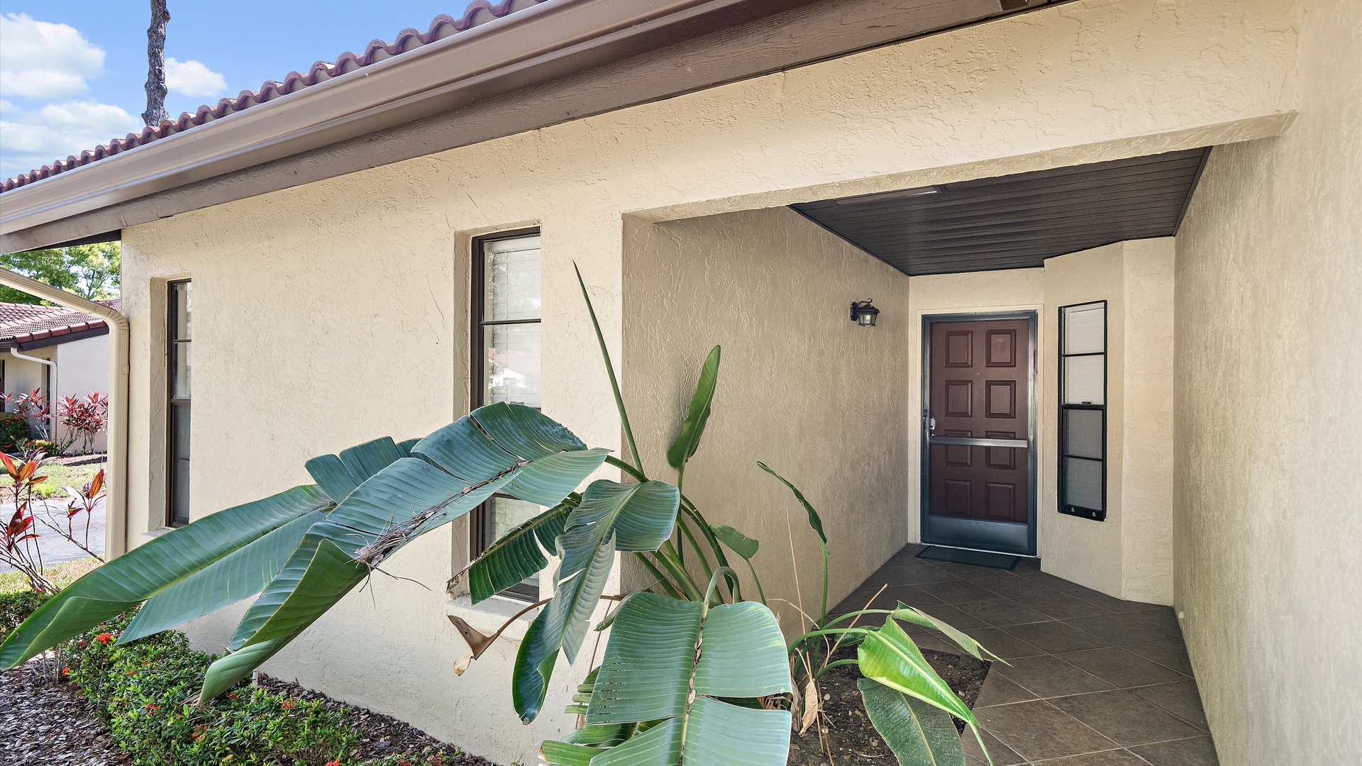 A welcoming tropical entrance marks your arrival, with lush banana plants greeting you at the covered entryway of this charming property.