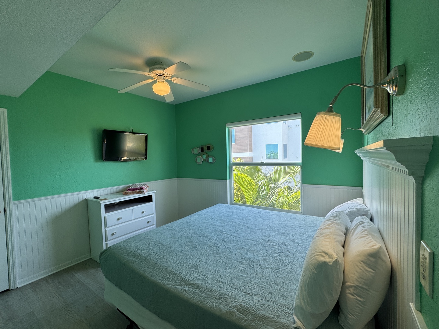 Your coastal bedroom awaits with refreshing turquoise walls and tropical palm views right outside your window. Relax under the ceiling fan after a day at the beach.
