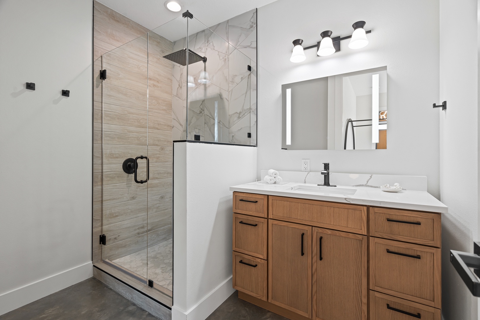 Step into this spa-like bathroom with a stunning walk-in shower featuring elegant marble and wood-tone tile, paired with a modern vanity offering ample storage for your getaway essentials.