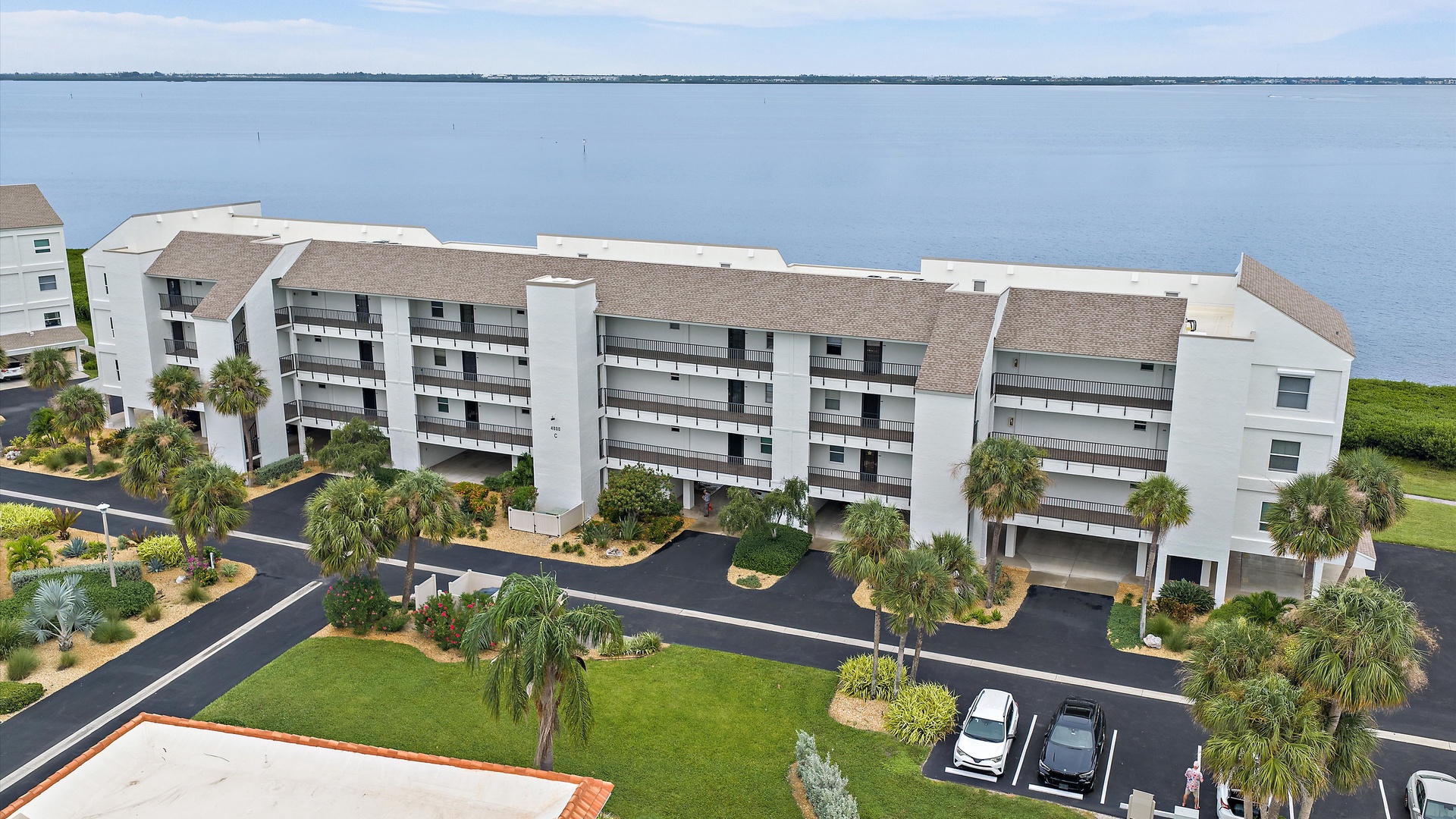 Sarasota Bay stretches behind Windward Bay’s waterfront buildings, with palms and landscaped grounds along the shore. The setting brings open water and coastal greenery together in one inviting view.