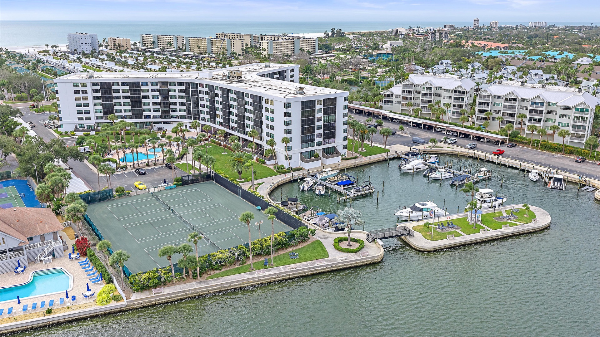 Aerial view of a waterfront resort complex featuring marina access, tennis courts, and swimming pools along the coastline.